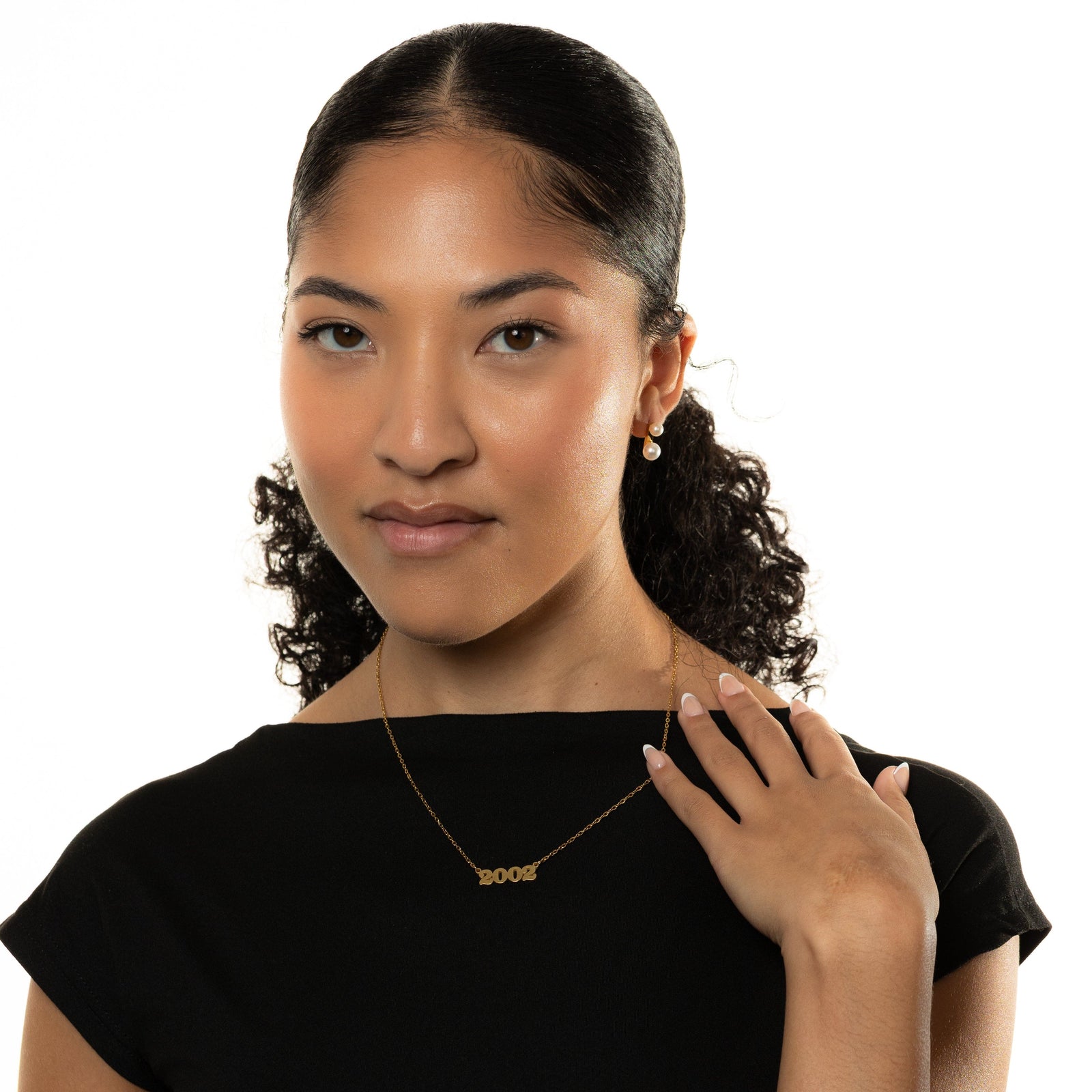 Woman wearing a black top and gold english birth year necklace with a pendant that reads 2002, on a white background