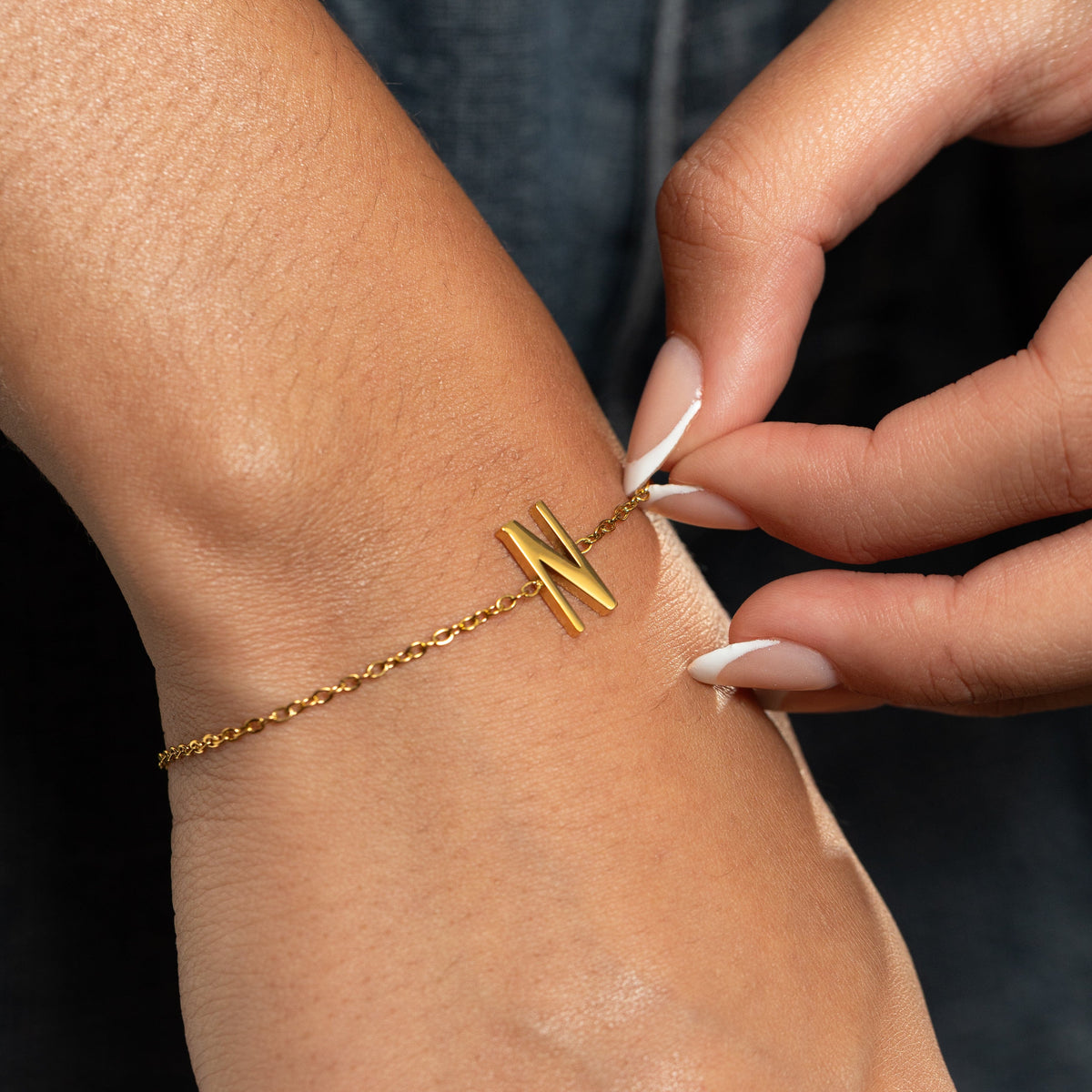 Gold bracelet with a letter 'N' pendant worn on a wrist.
