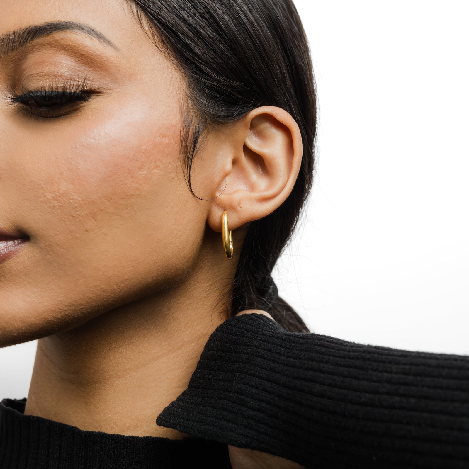 Close up of the gold Essential Oval Hoops as worn by the model on their right ear.