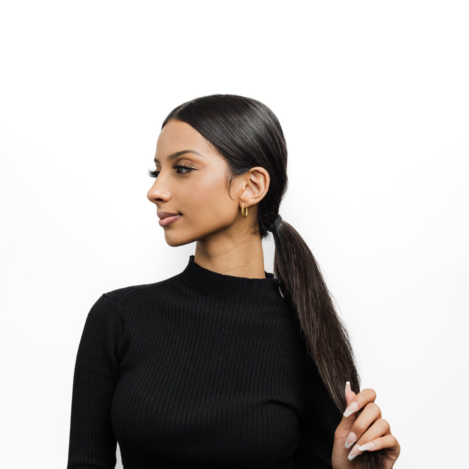 Photo of the model looking to their right and holding their tied hair with their left hand. The model is wearing the gold Essential Oval Hoops on their left ear.