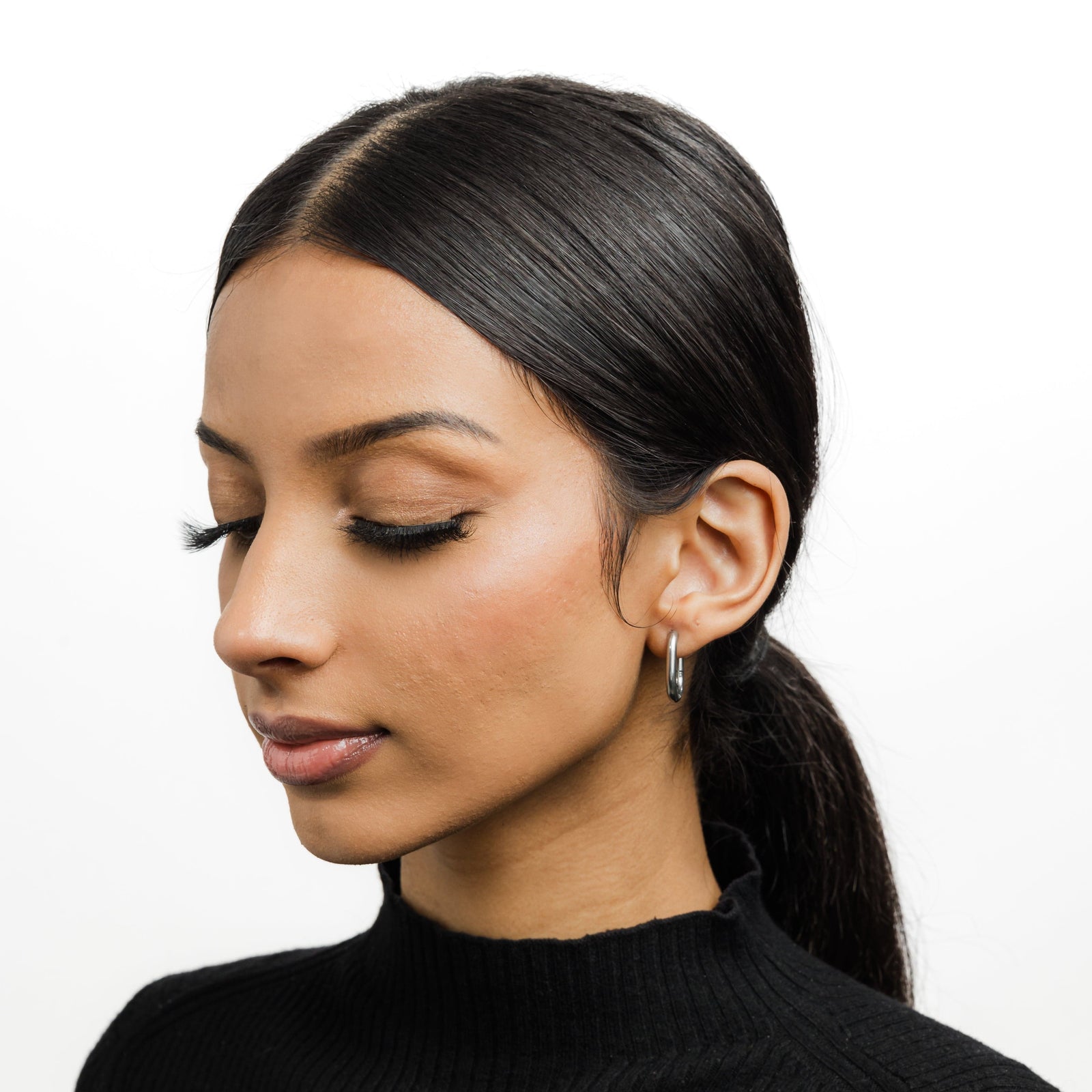 Photo of the model looking down, the model is wearing the silver Essential Oval Hoops on their left ear.