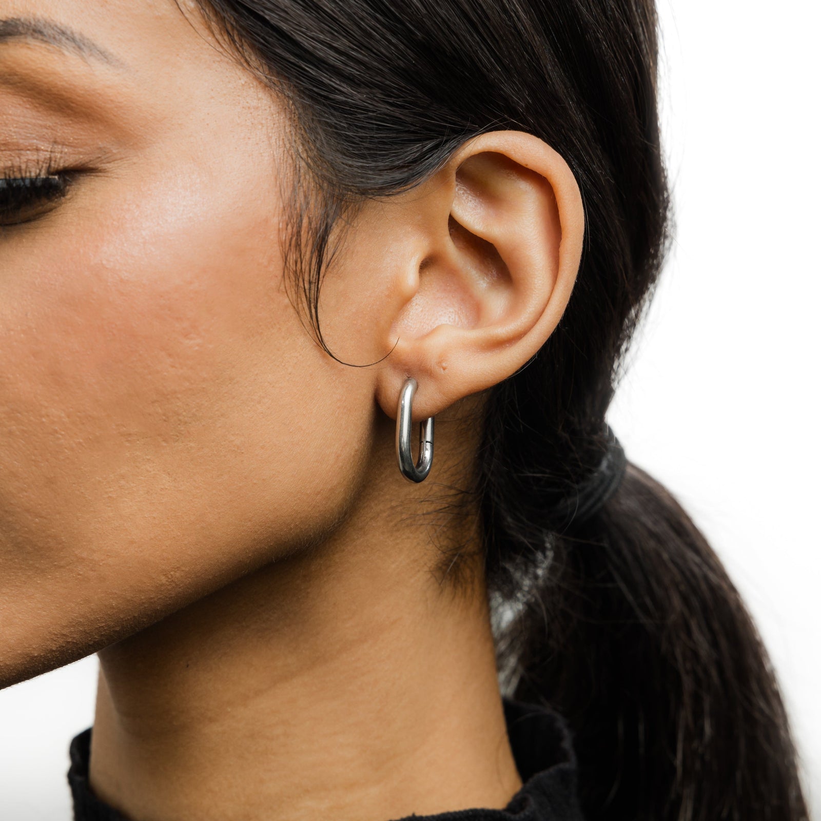 Close up of the silver Essential Oval Hoops as worn by the model on their left ear.