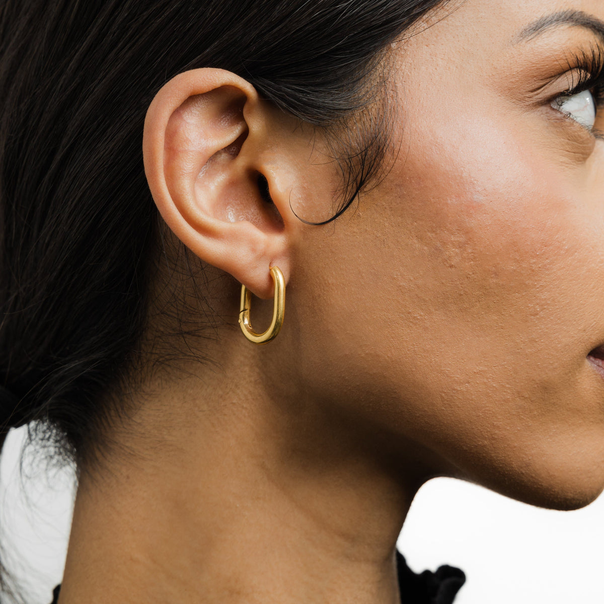 Close up of the gold Essential Oval Hoops as worn by the model on their right ear.