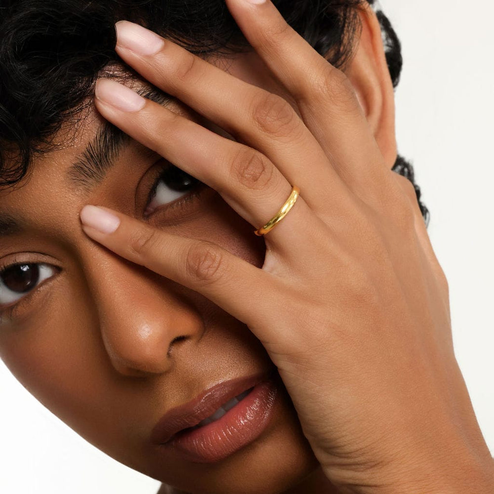 Close up of the model's face with their left hand touching the left side of their face. The model is wearing the  Essential Ring | Thin on their left ring finger.