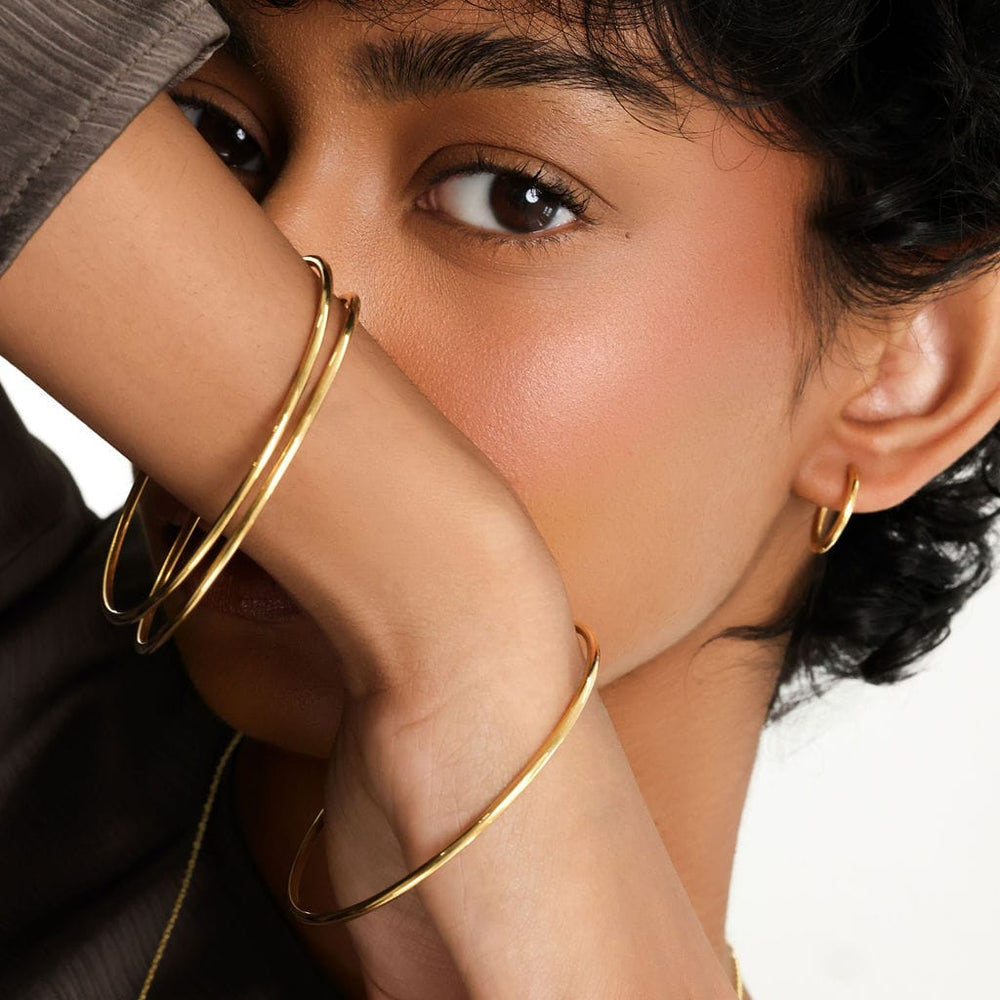 Photo of the model wearing three pieces of gold Essential Thin Bangle