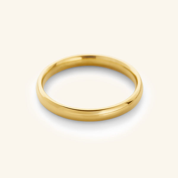 A minimalist, highly polished 18k gold-plated classic band ring resting on a soft cream background.