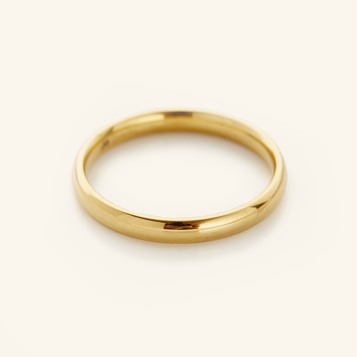 Gold band ring displayed on a soft cream background.