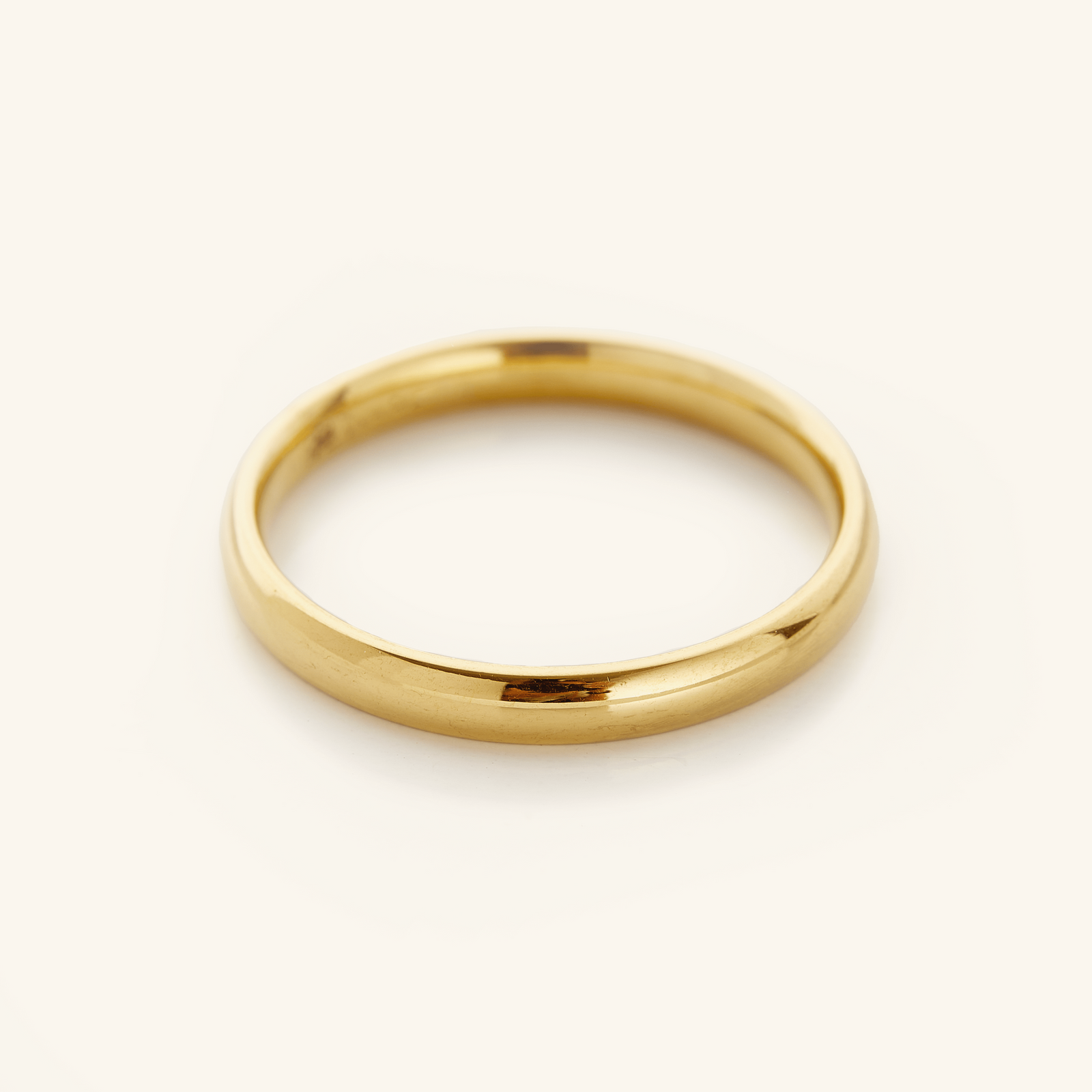 Gold band ring displayed on a soft cream background.