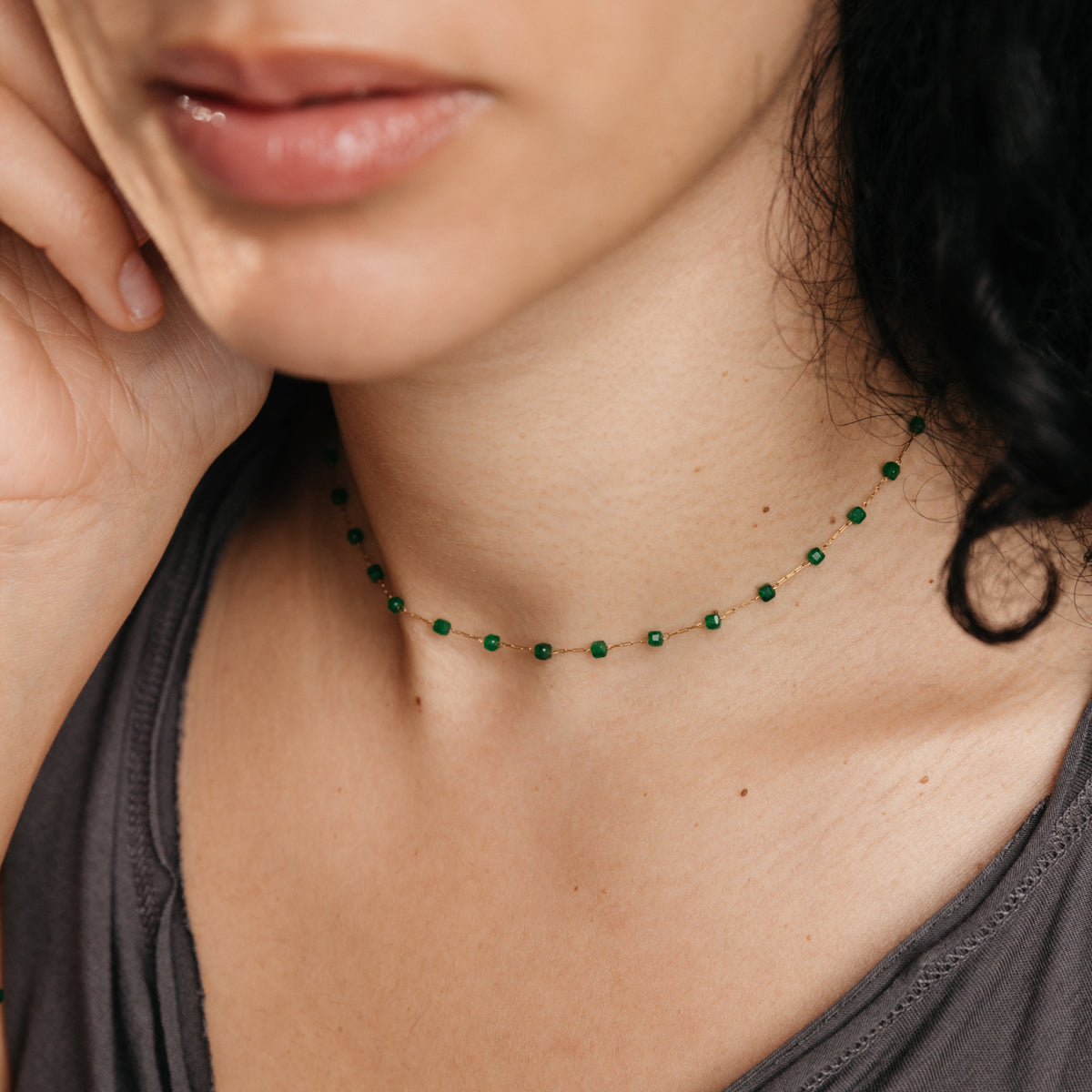 On-model lifestyle view of the Essential Emerald Micro Chain, featuring a delicate 18k gold-plated chain dotted with faceted green emerald beads worn close around the neckline.