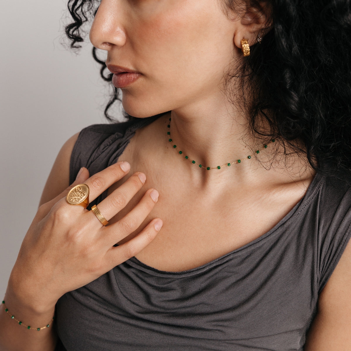Model styled in 18k gold-plated Nominal jewelry featuring the Essential Emerald Micro Chain, Essential Emerald Micro Bracelet, Palestinian Olive Huggie Hoops, and the Alhamdulillah Signet Ring.