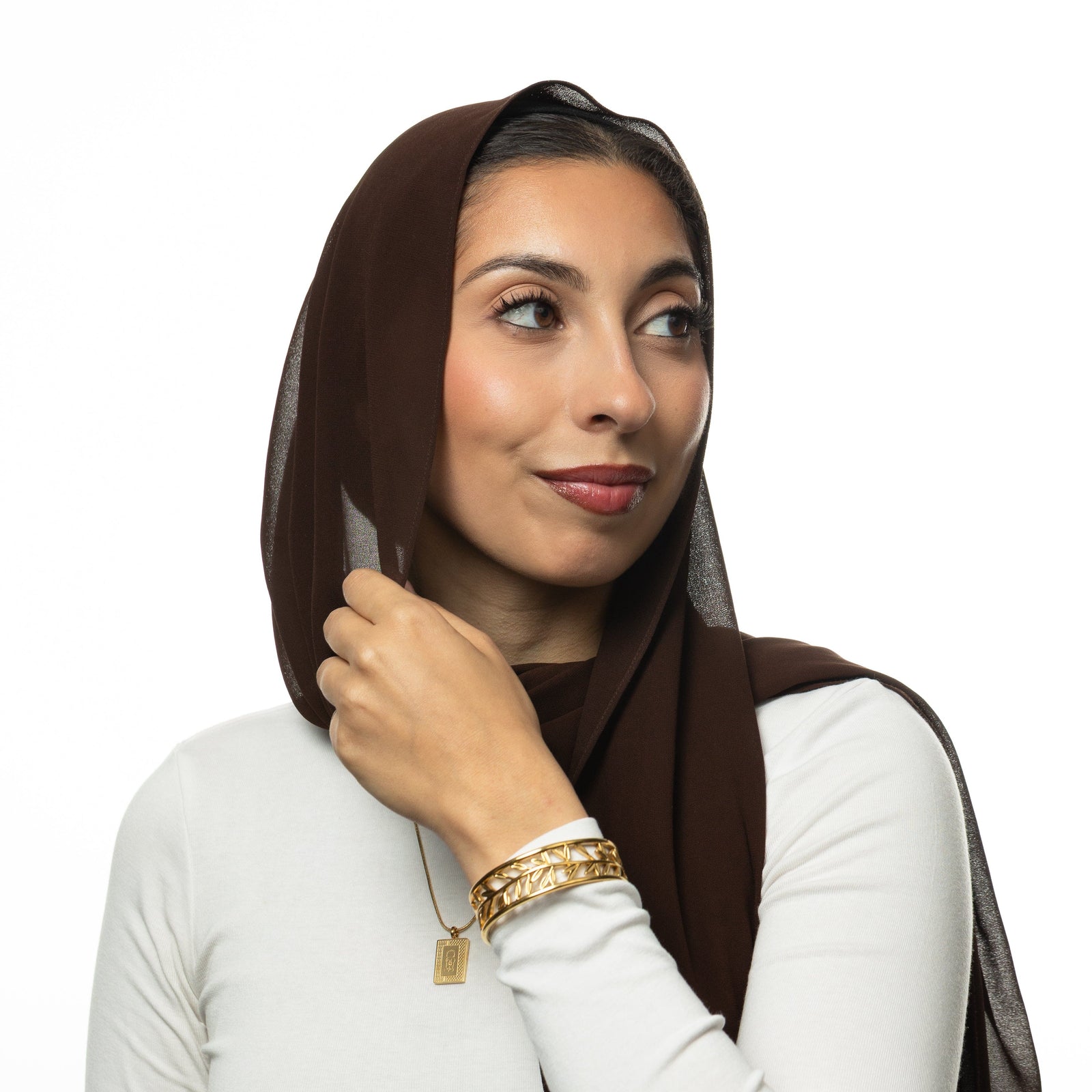 Woman wearing a brown hijab, white long sleeves shirt, gold necklace, and gold Eternal bangle.