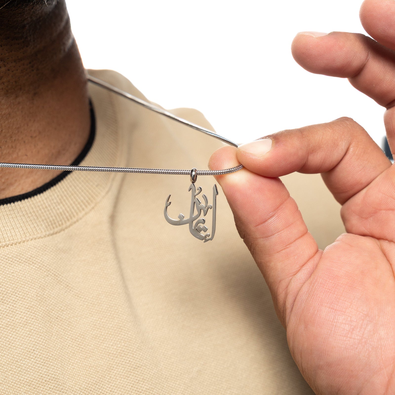 Man holding up a silver 'Faith' calligraphy necklace across his chest.
