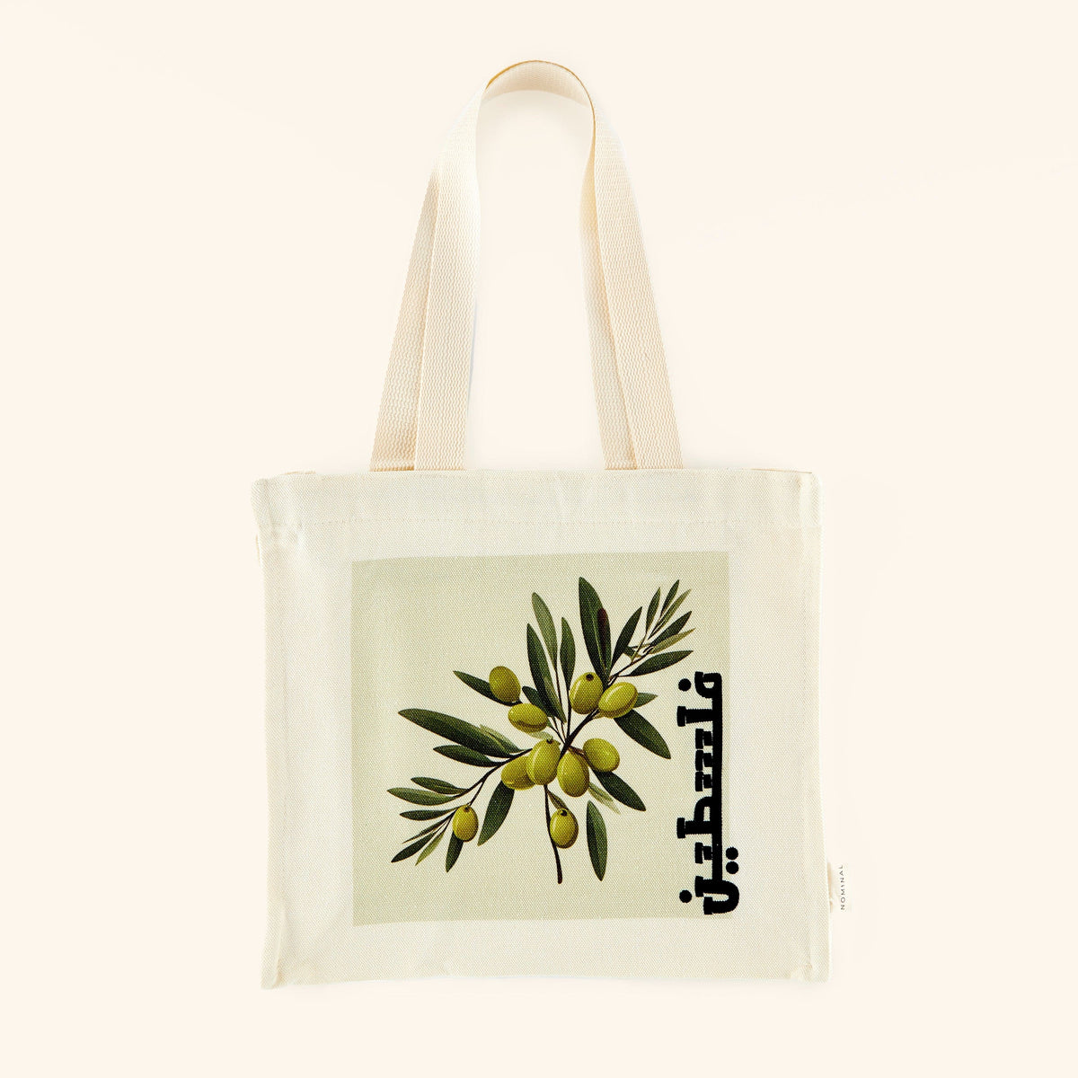 A textured cotton canvas tote bag featuring a vibrant olive branch print and the word "Palestine" elegantly scripted in Arabic. The tote measures 13 inches in height, 12 inches in width, and 3.5 inches in depth, with an 11-inch strap drop. It includes a zip closure and one open interior pocket.