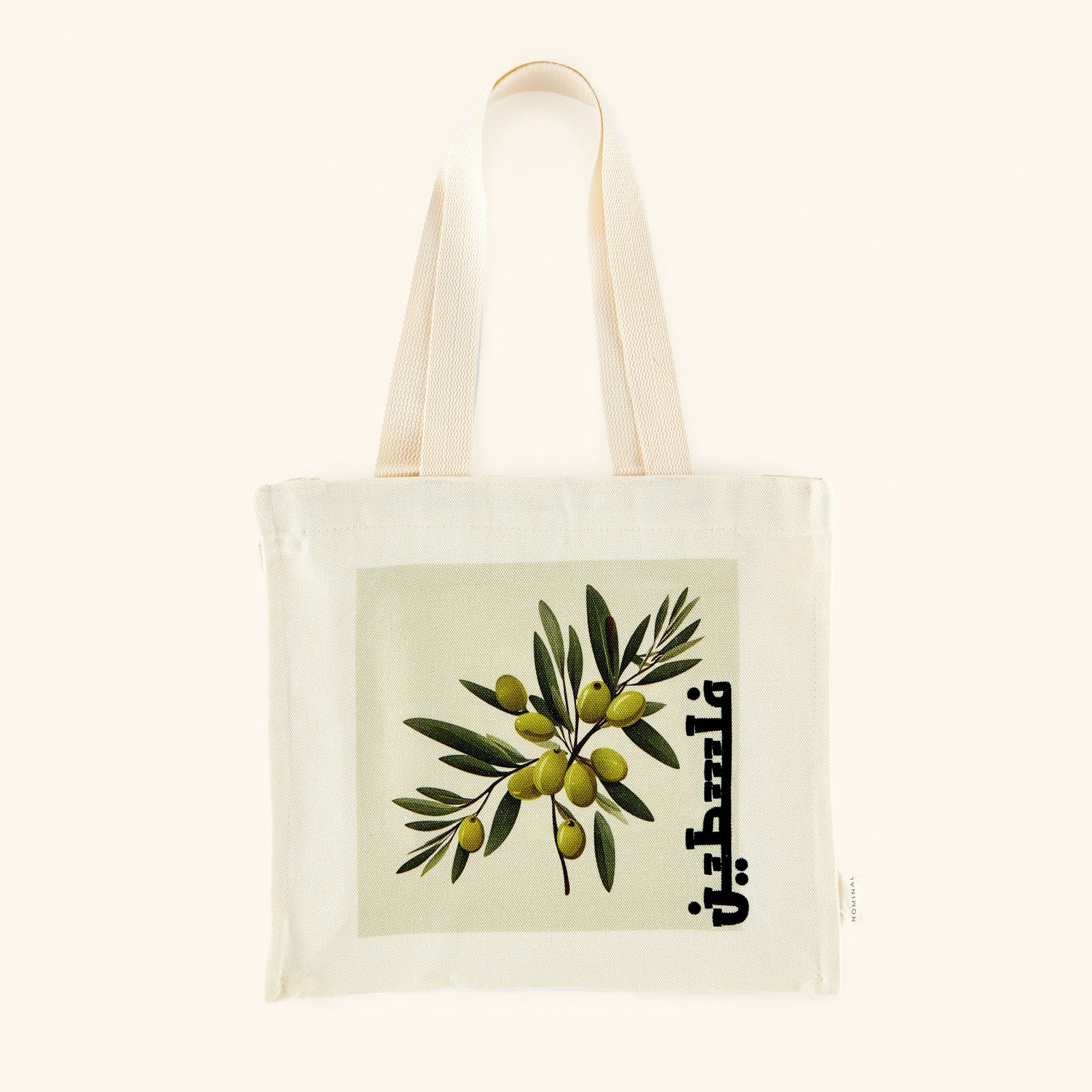 A textured cotton canvas tote bag featuring a vibrant olive branch print and the word "Palestine" elegantly scripted in Arabic. The tote measures 13 inches in height, 12 inches in width, and 3.5 inches in depth, with an 11-inch strap drop. It includes a zip closure and one open interior pocket.