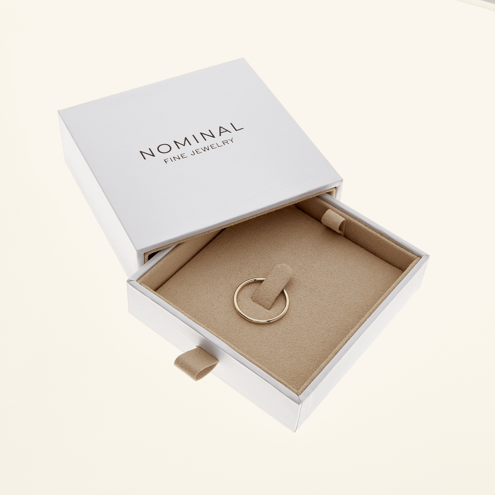 Thin gold band displayed inside a Nominal Fine Jewelry box with beige velvet interior.