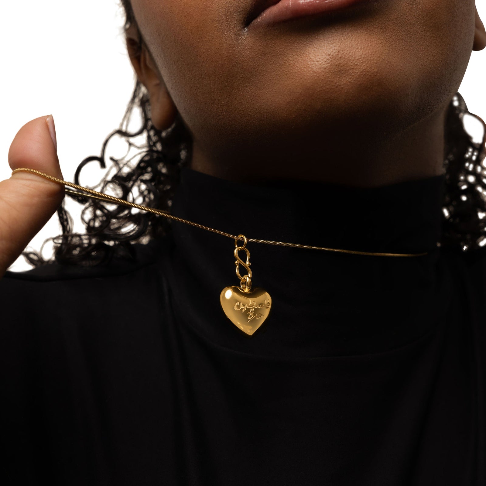 Model pulls the thin gold plated chain of the "Free Palestine" Heart Necklace. The gold plated puffed heart pendant hanging.