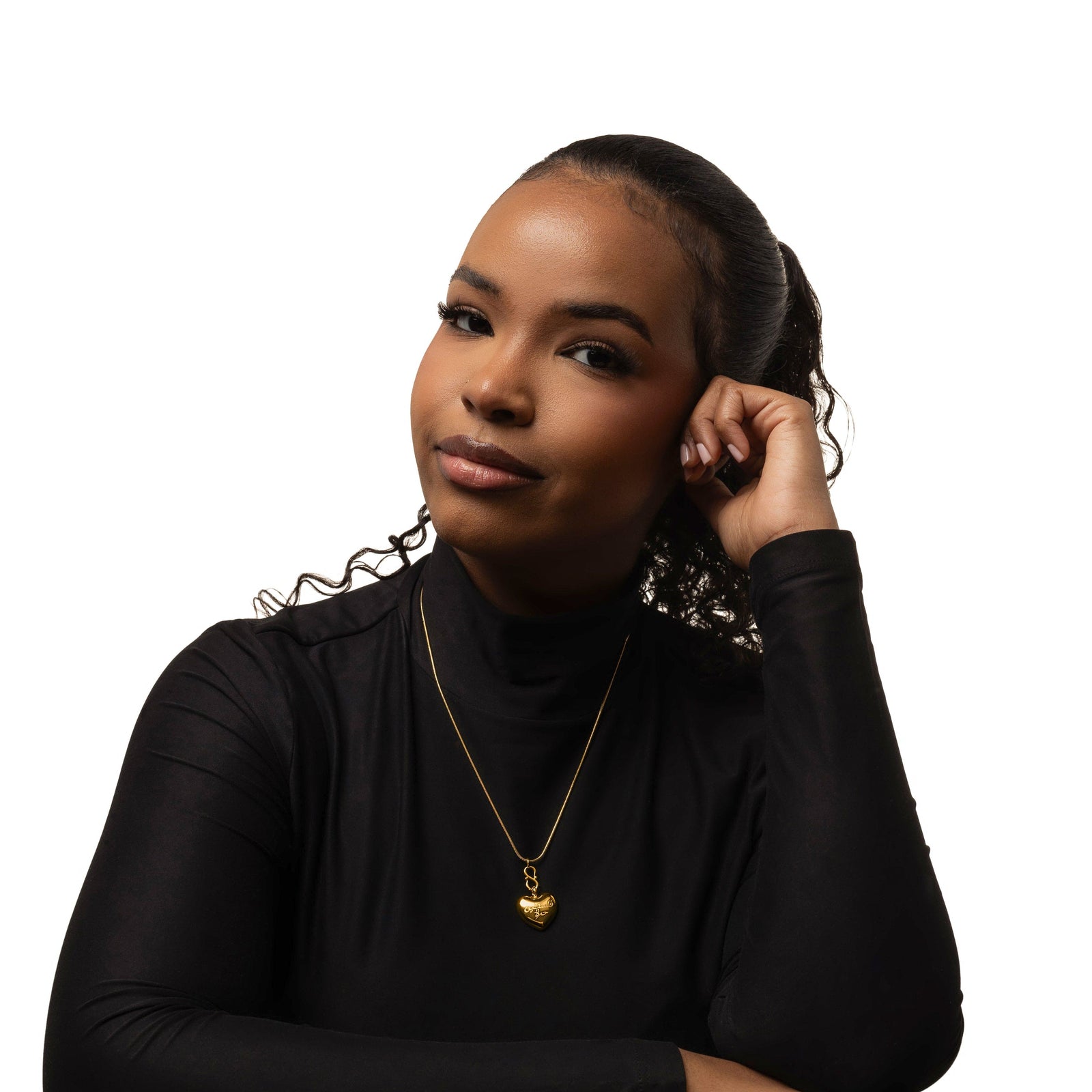 Photo of the model wearing a fitted black long-sleeve top with a high neckline. A gold necklace with a small heart-shaped pendant rests at the center of her chest.