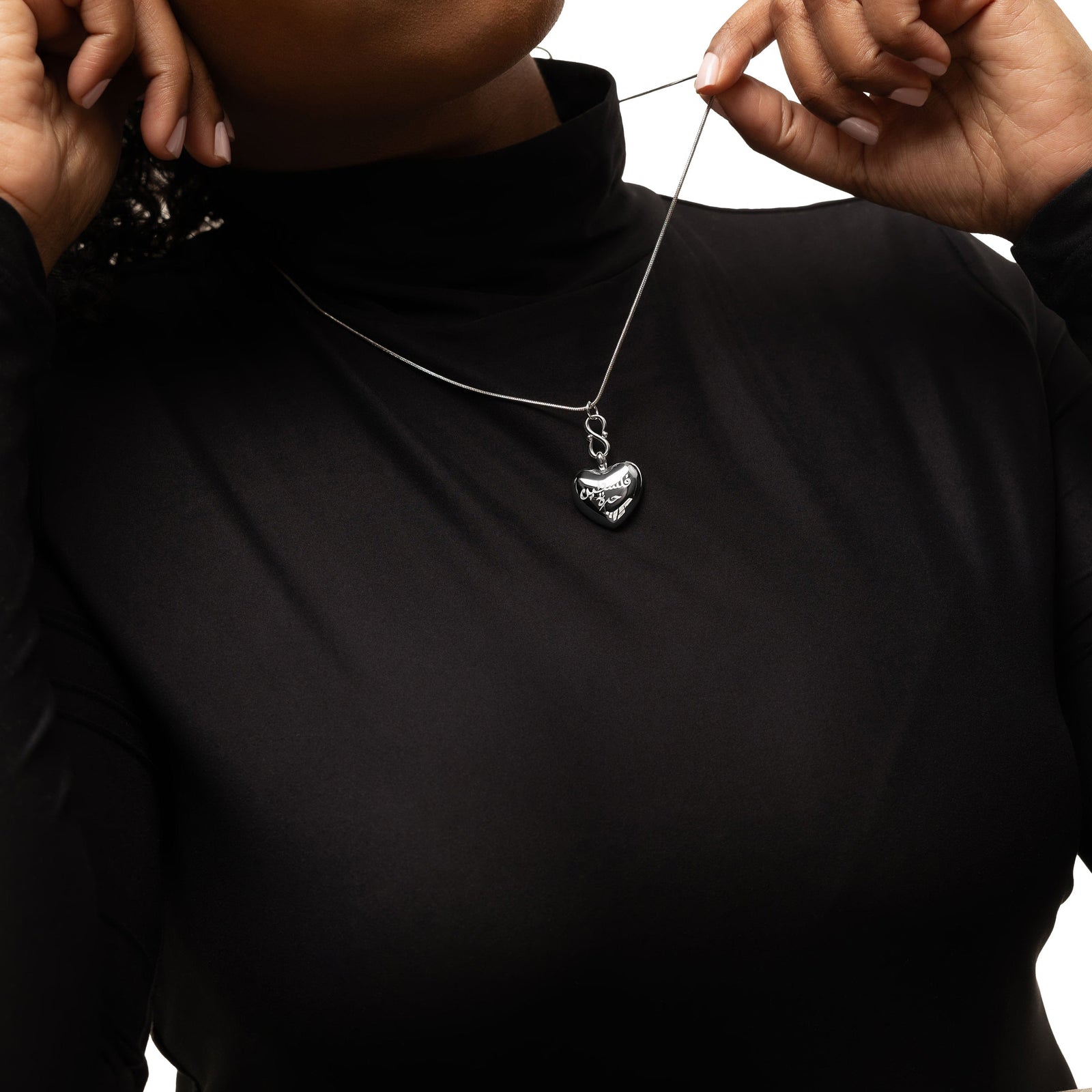 Photo of the model pulling the thin chain of the silver "Free Palestine" Heart Necklace, the silver puffed heart pendant hanging at the bottom.