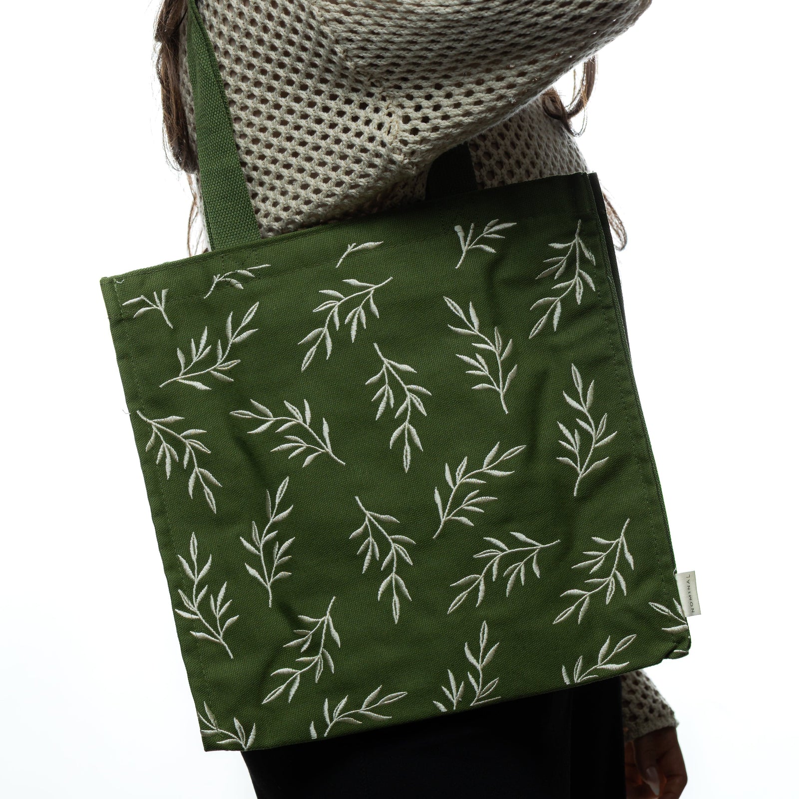 Woman wearing the tote over her shoulder. The embroidered olive branch pattern is clearly displayed on the green fabric.