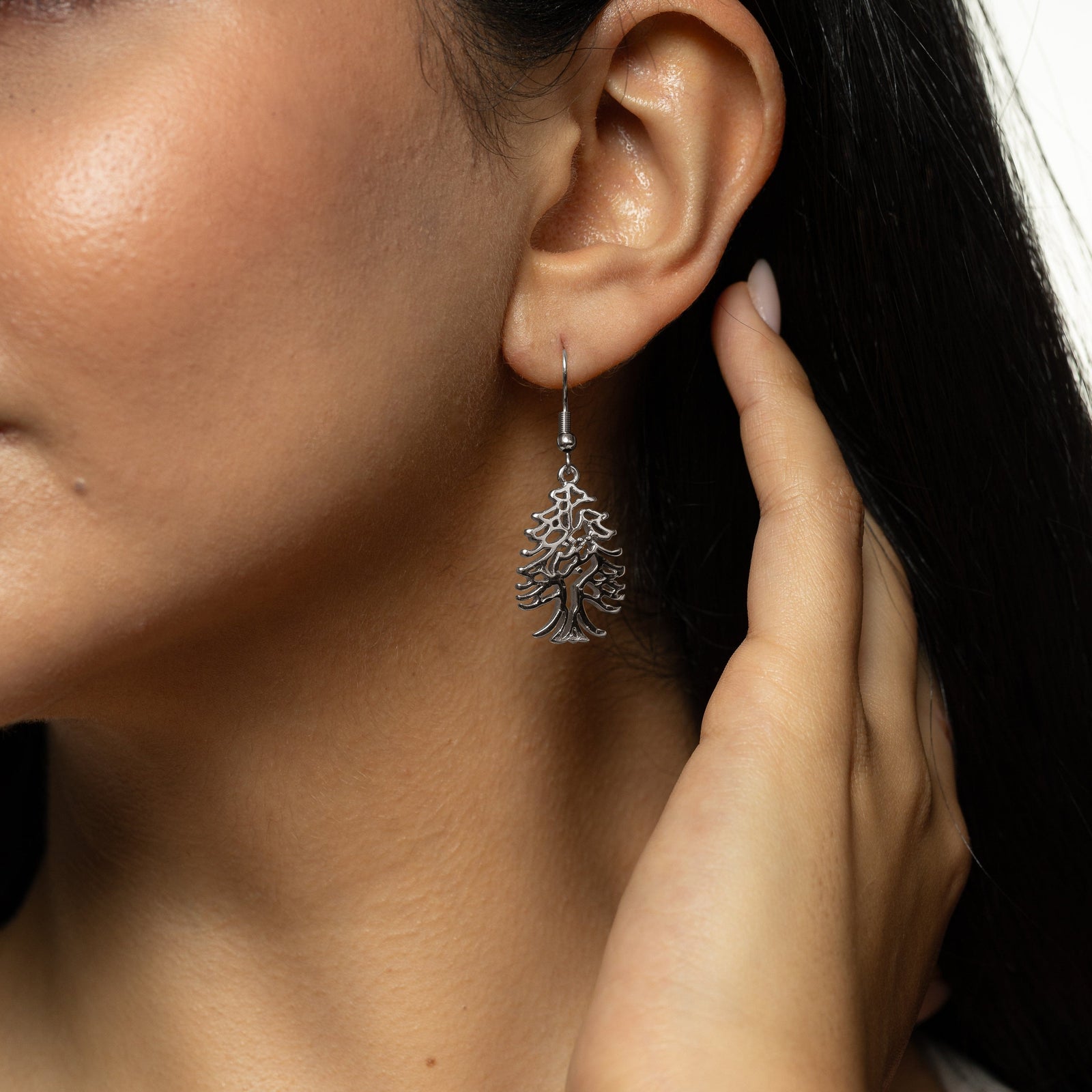 Model holds their hair away from their left ear showing the dangling Freedom is the Soul Cedar silver earring.