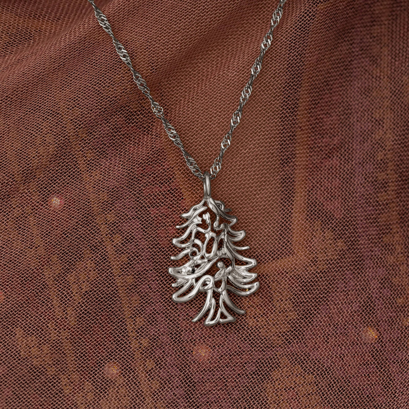 Close up photo of the silver necklace focusing on the pendant as it rests on a fabric.