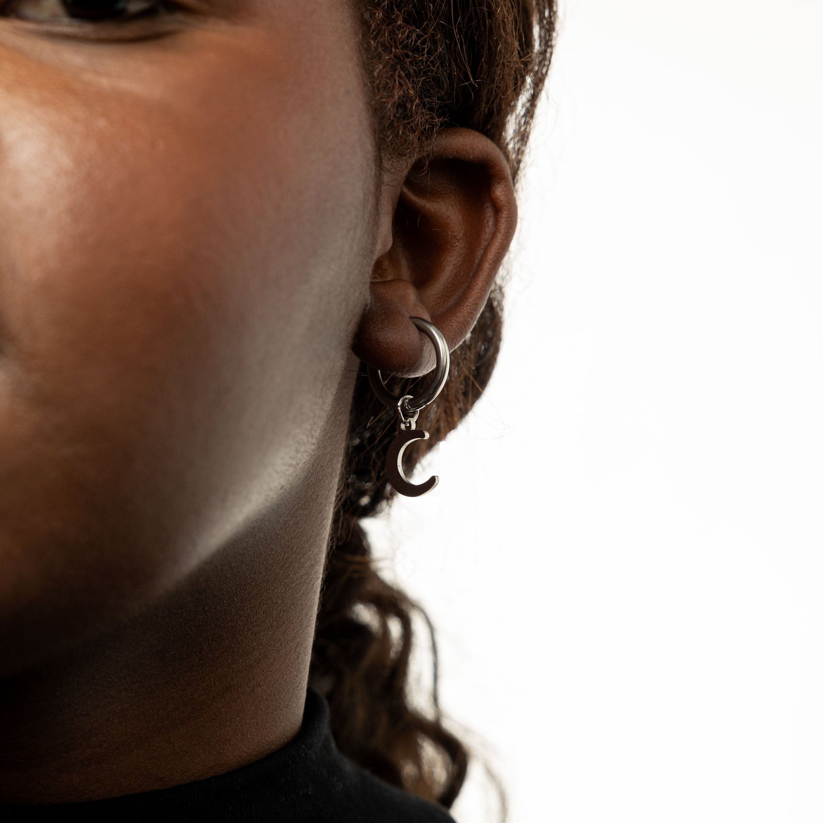 Close up of the silver Galaxy Hoop Earring with crescent moon charm as worn by the model on their left ear.