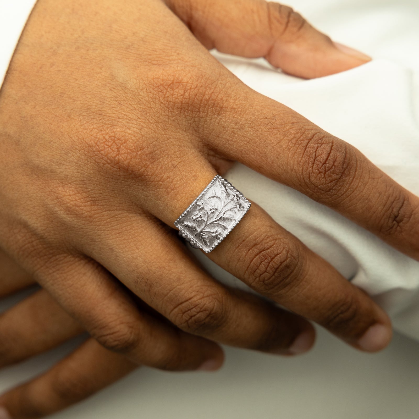 Close-up of the silver Garden Ring worn on a hand against a white sleeve, showing its intricate floral engravings.