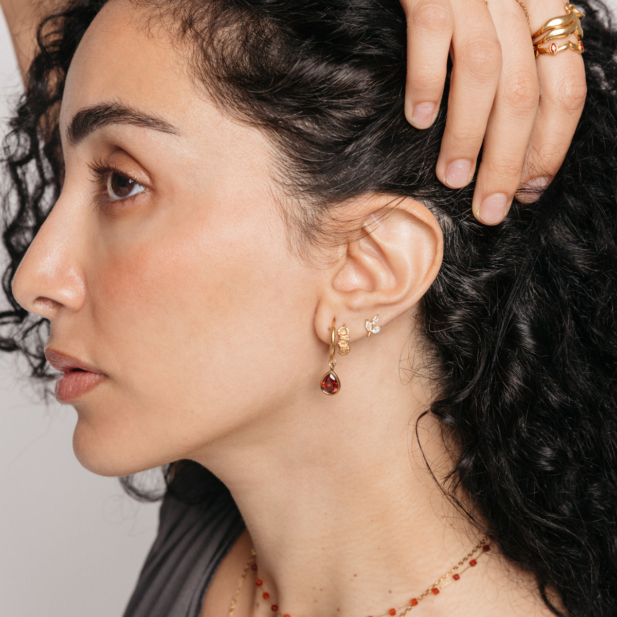 Model styled in 18k gold-plated Nominal jewelry featuring an ear stack with the Palestinian Olive Huggie Hoops paired with the Garnet Stone Huggie Hoops and Pavé Olive Branch Studs.