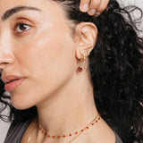 Model styled in 18k gold-plated Nominal jewelry featuring an ear stack with the Palestinian Olive Huggie Hoops paired with the Garnet Stone Huggie Hoops and Pavé Olive Branch Studs.