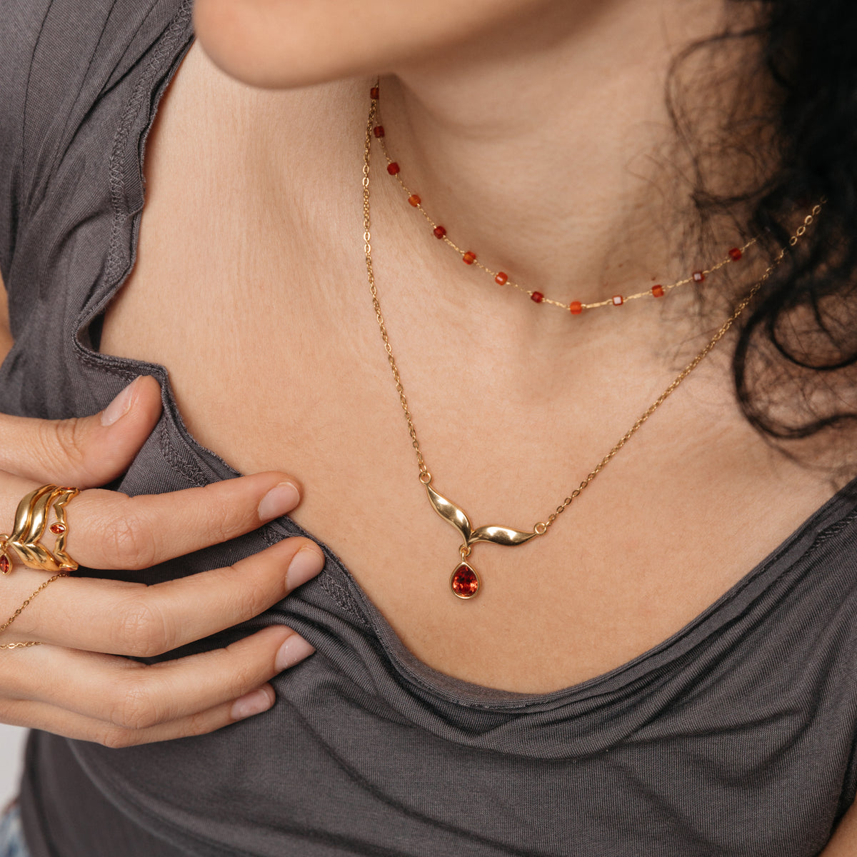 Model styled in 18k gold-plated Nominal jewelry featuring the Garnet Stone Keffiyeh Necklace layered with the Essential Red Agate Micro Chain