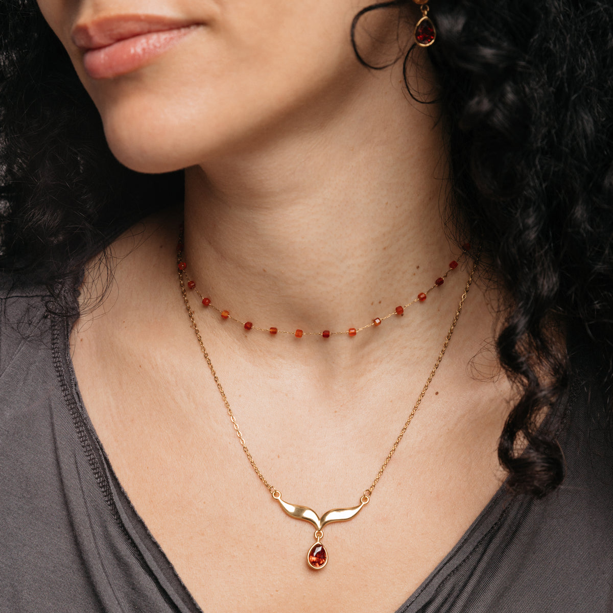 Model styled in 18k gold-plated Nominal jewelry featuring the Garnet Stone Keffiyeh Necklace layered with the Essential Red Agate Micro Chain.