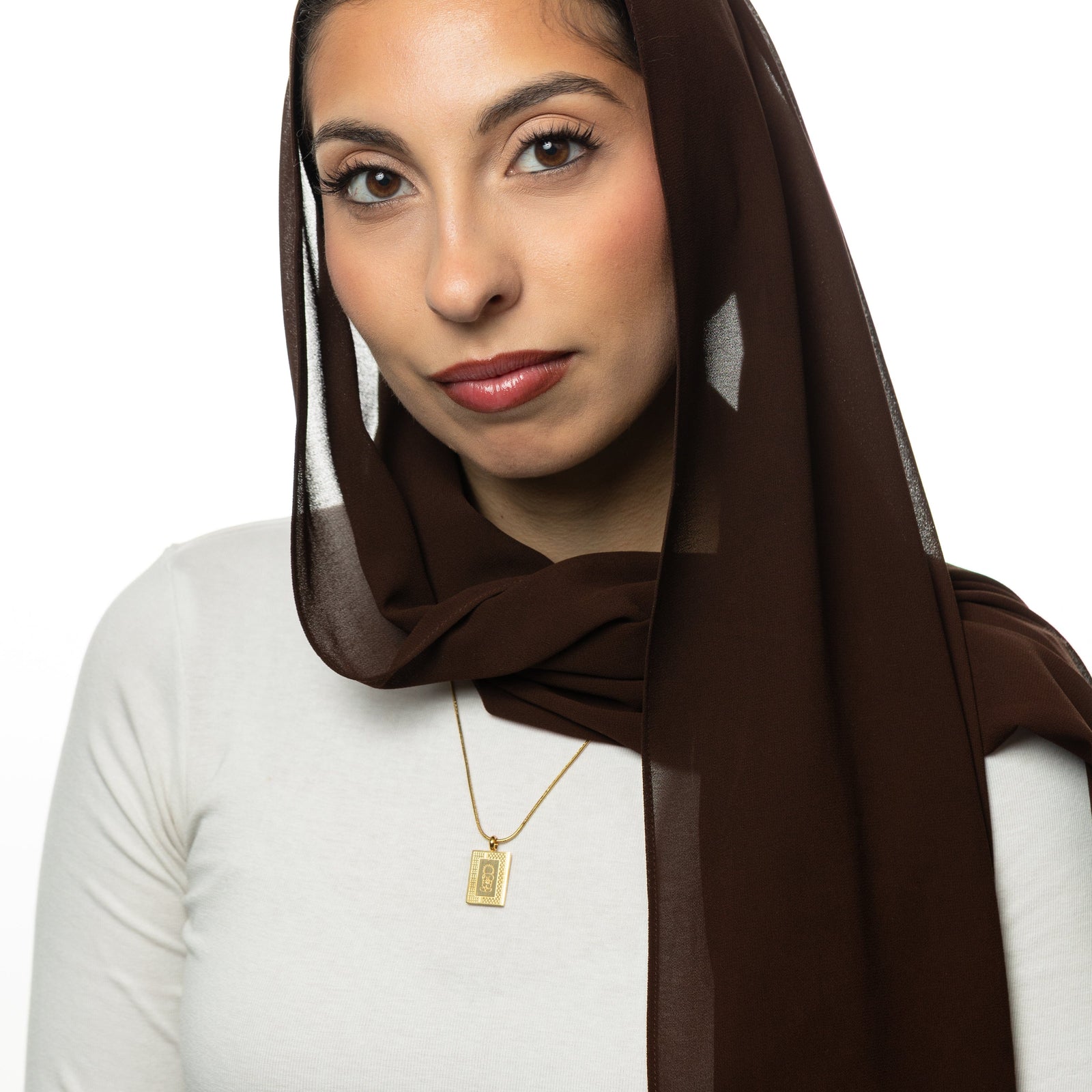 Woman wearing a brown hijab, white shirt, and gold Handala Necklace on a white background