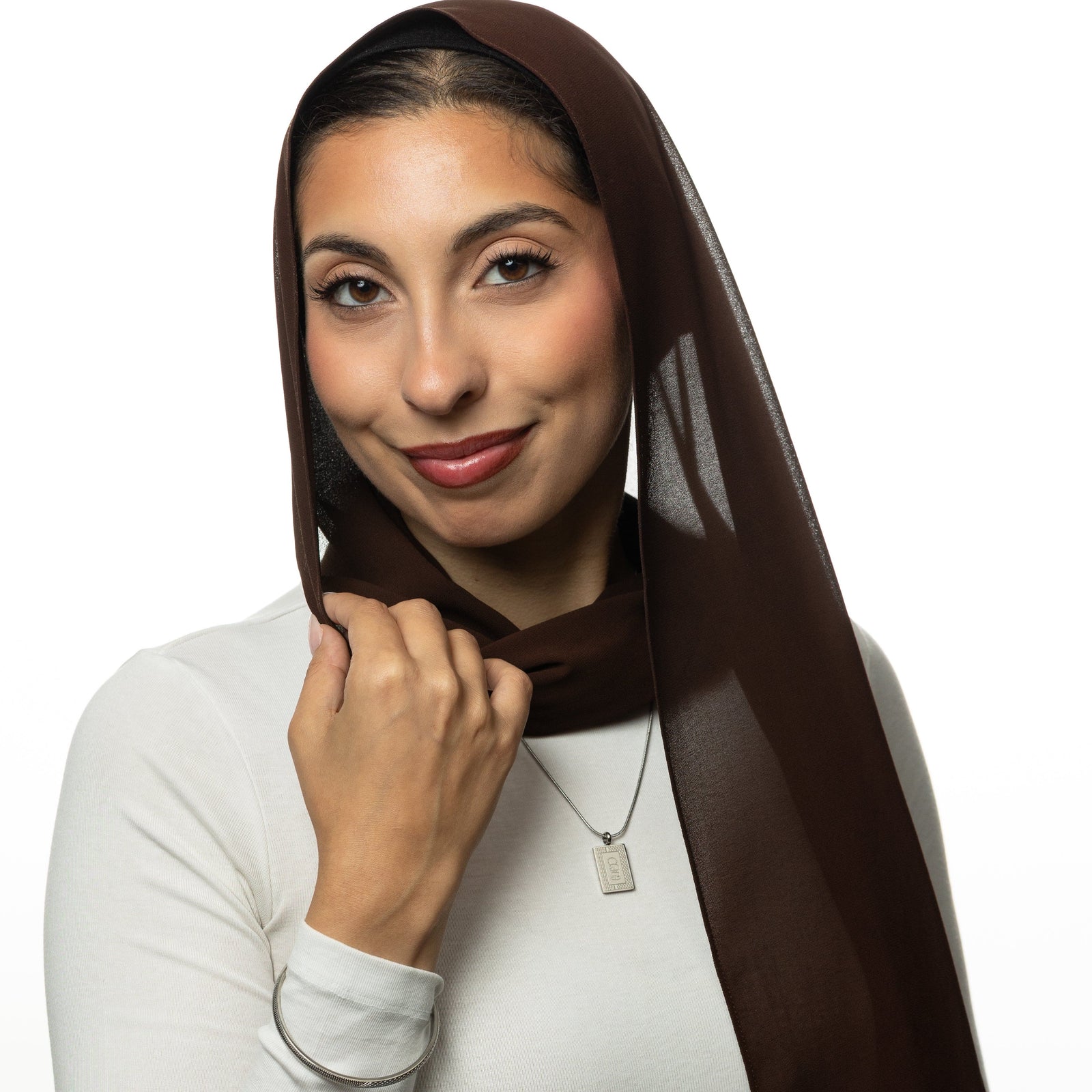 Woman wearing a brown hijab, white shirt, and silver Handala Necklace