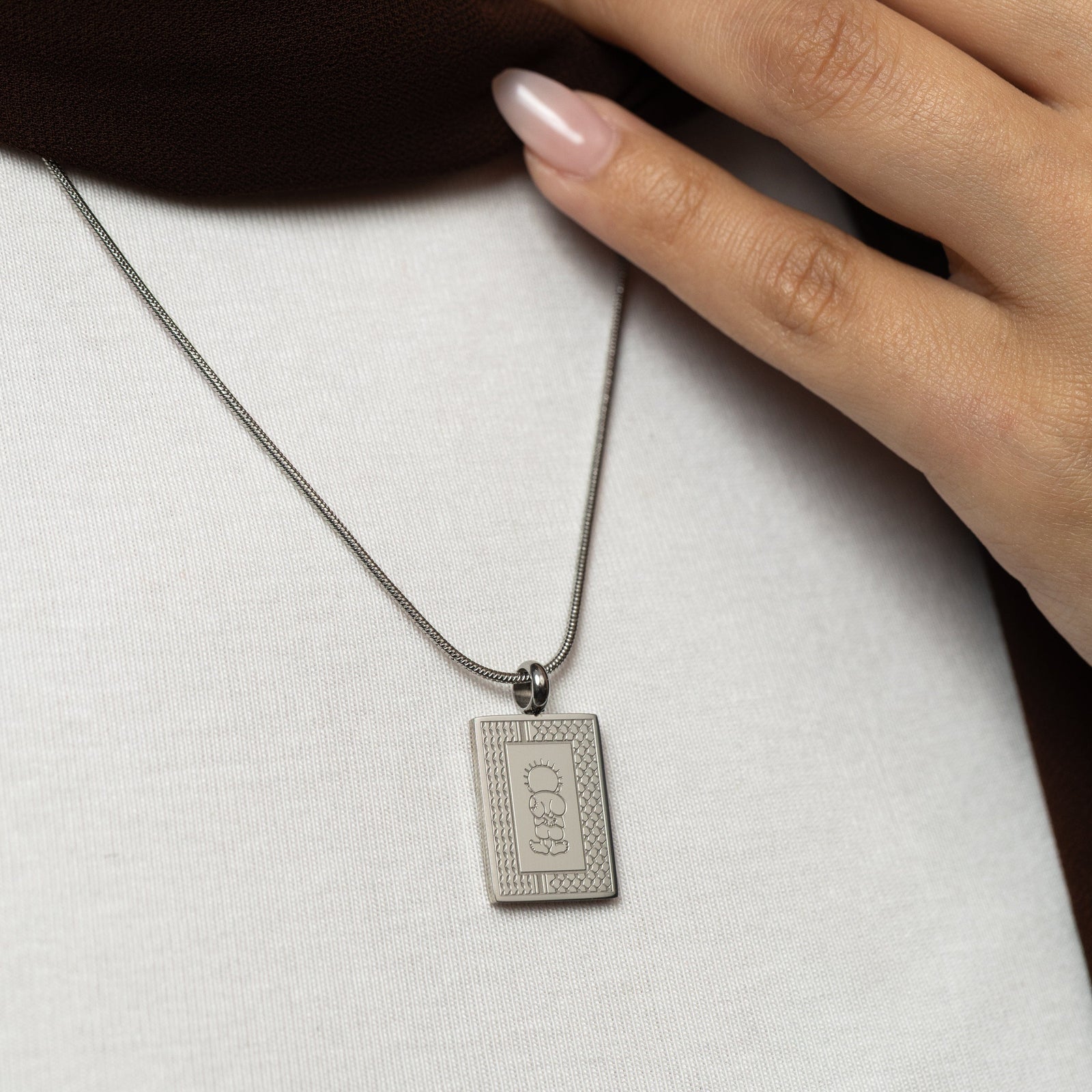 Silver Handala Necklace worn by a woman, hand gently on the brown scarf.