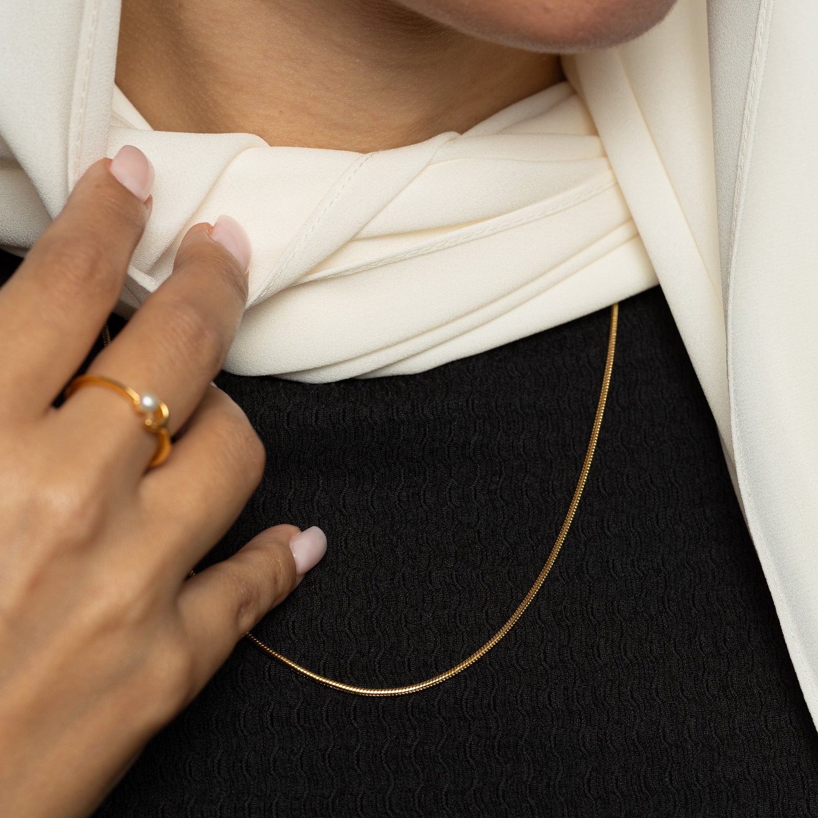 Close-up of a person wearing a gold harmony necklace with a white scarf and black garment.