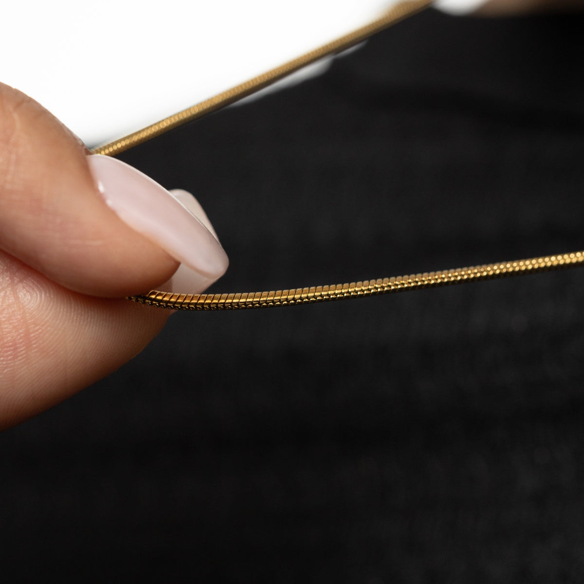 Gold harmony necklace held by a hand against a dark background