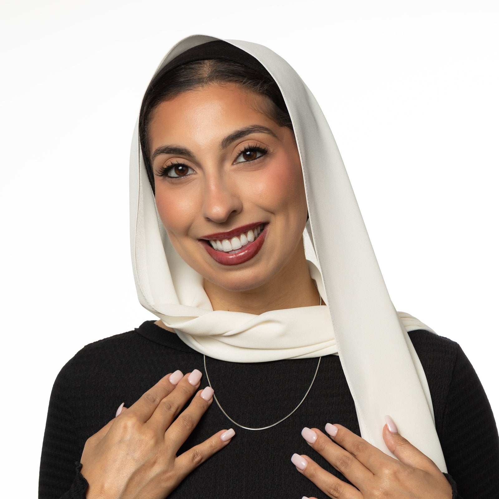 Woman wearing a white hijab, a black top, and a gold harmony necklace