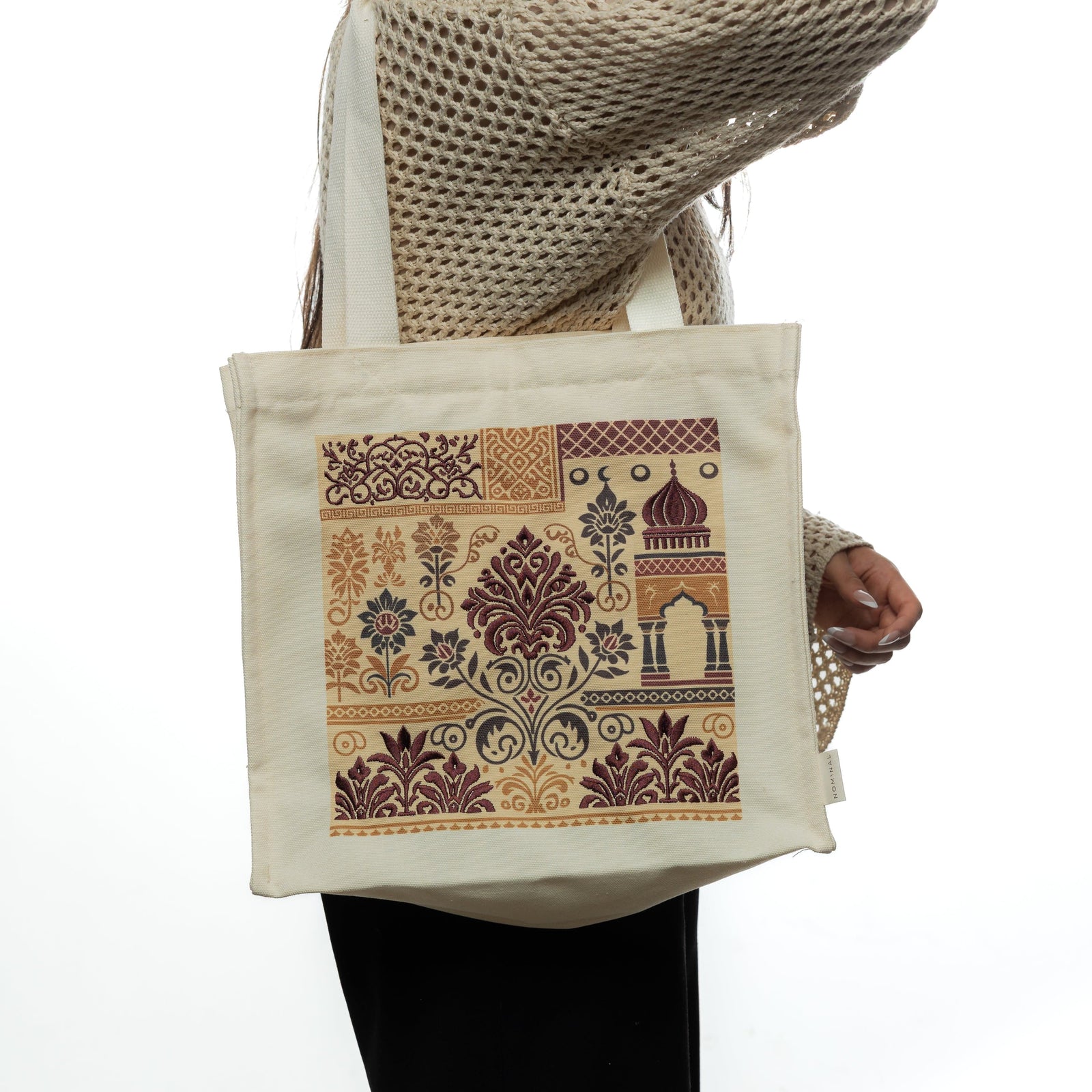 Person wearing a crochet sweater holds the heritage tote bag with detailed floral and mosque-inspired prints in maroon and gold.