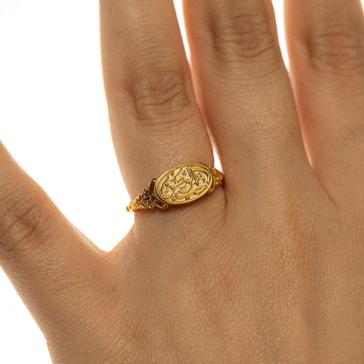 Woman wearing the gold Homeland Ring with Arabic calligraphy on the oval face in a close-up hand shot.