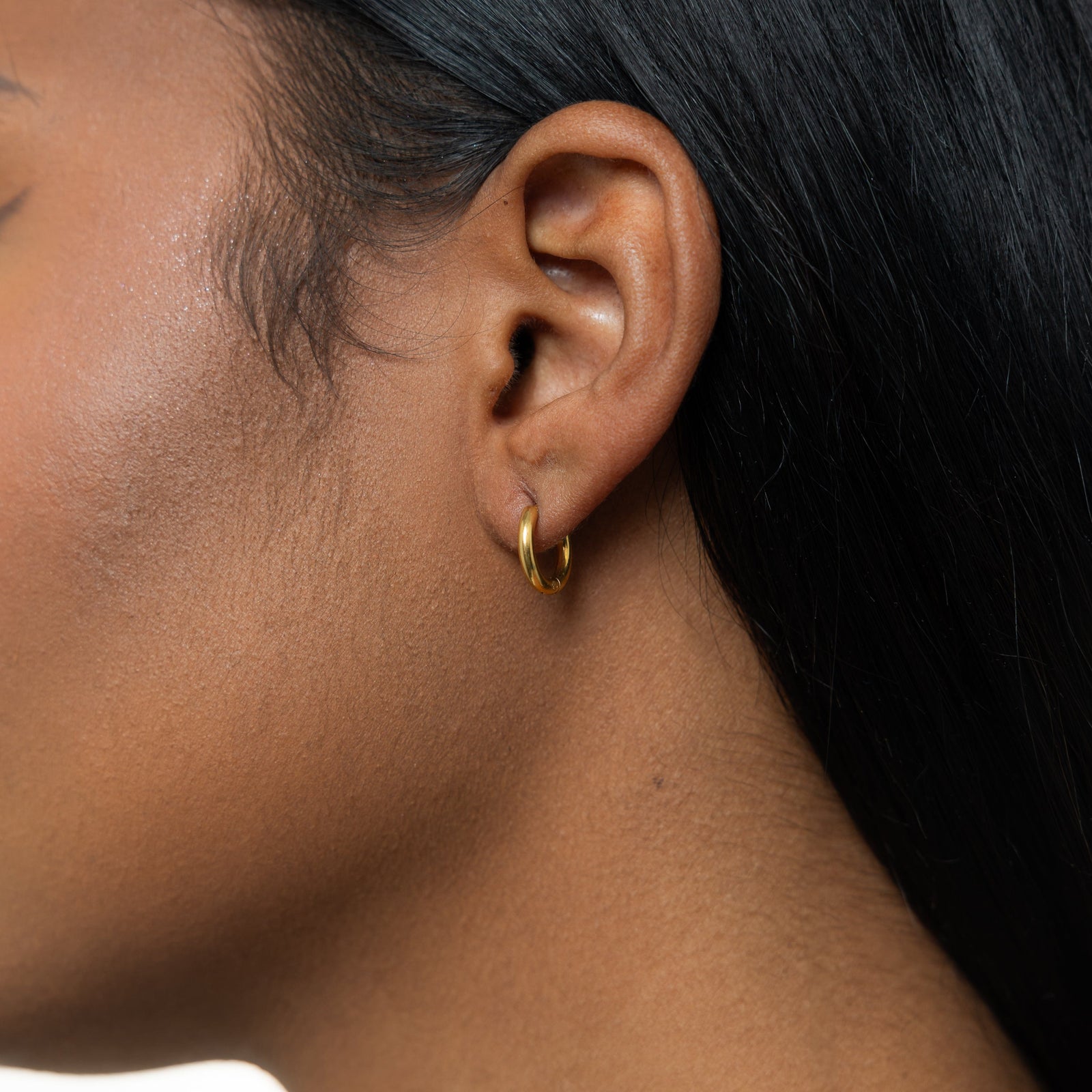 Close up of the gold Huggie Essential Hoops | 8mm as worn by the model on their left ear.