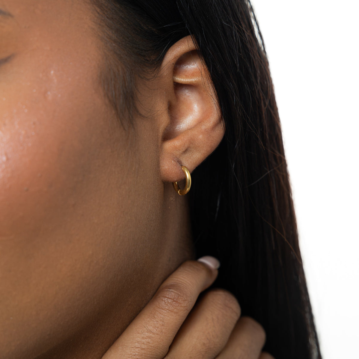 Close up of the gold Huggie Essential Hoops | 8mm as worn by the model on their left ear.