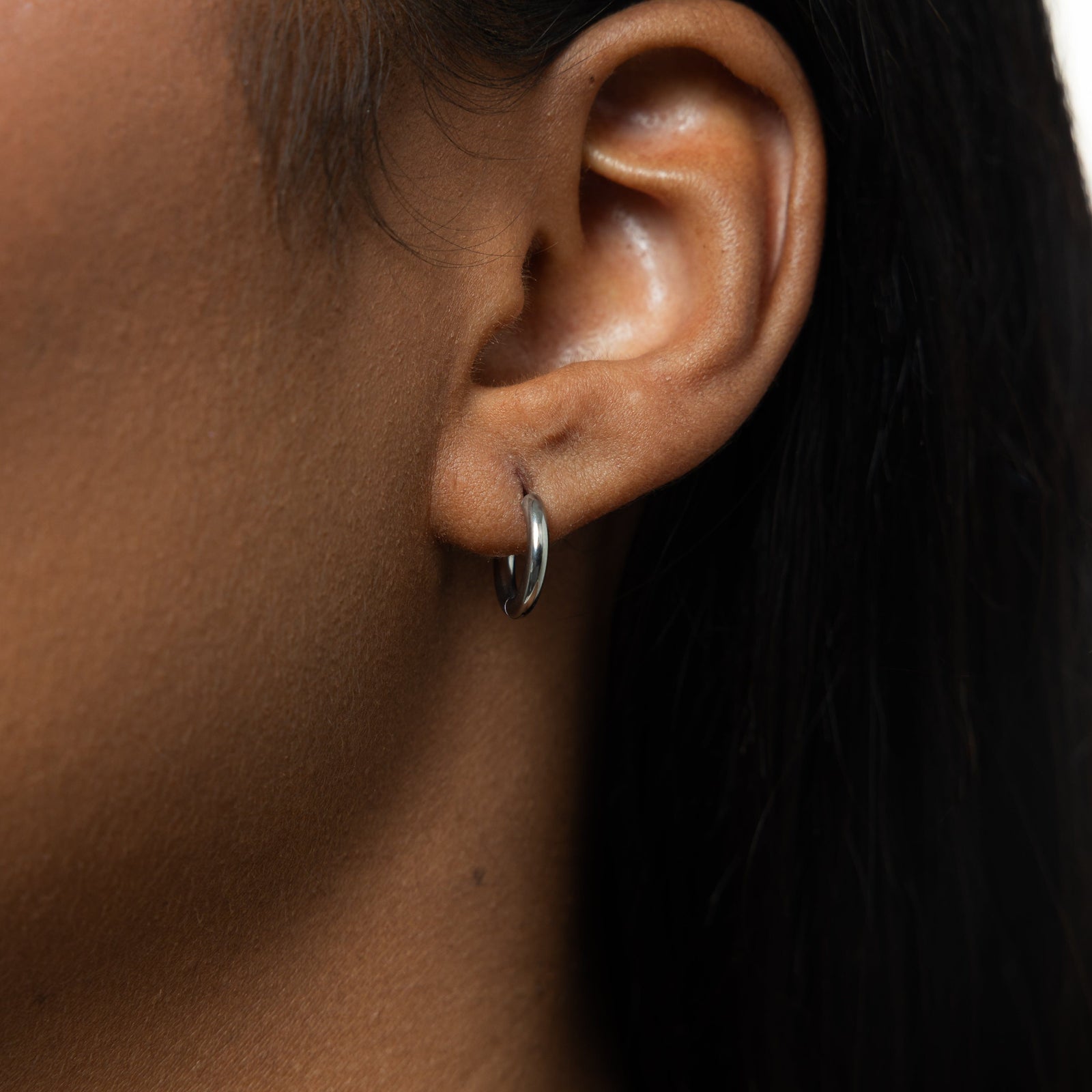 Close up of the silver Huggie Essential Hoops | 8mm as worn by the model on their left ear.