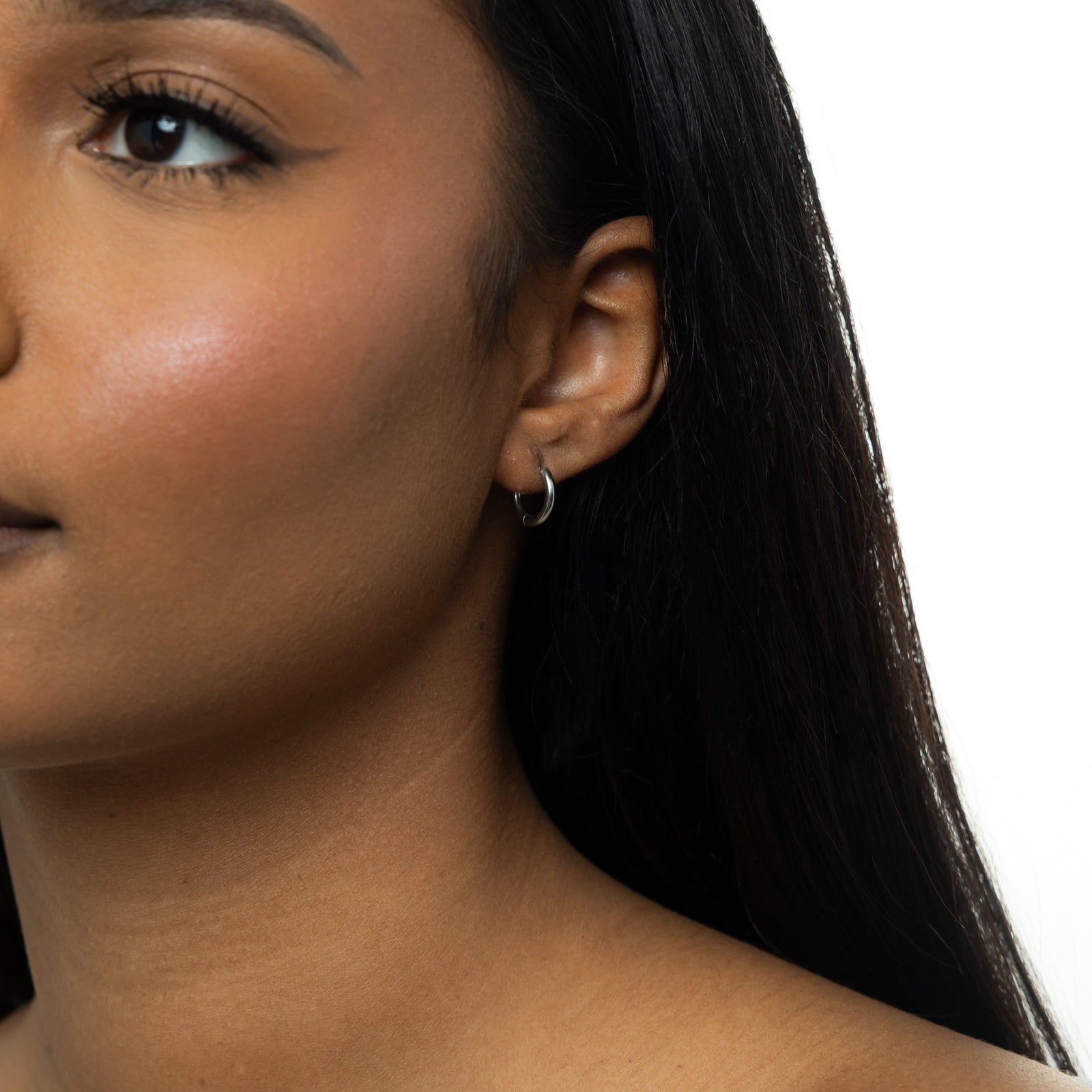 Close up of the silver Huggie Essential Hoops | 8mm as worn by the model on their left ear.