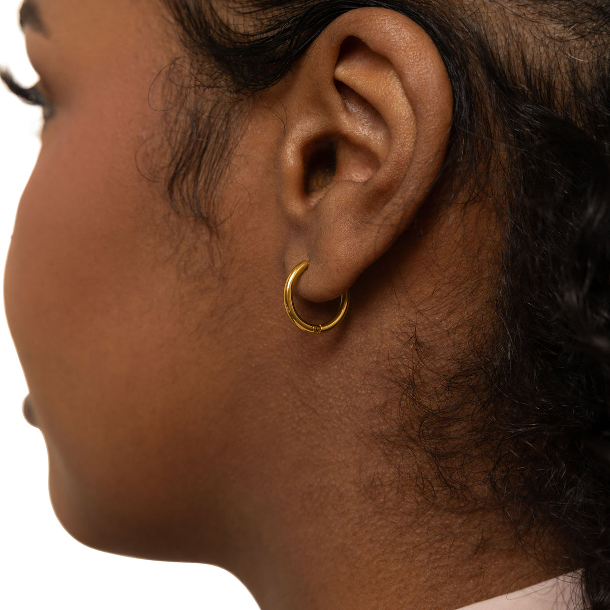 Close up of the gold Huggie Essential Hoops | 12mm as worn by the model on their left ear.