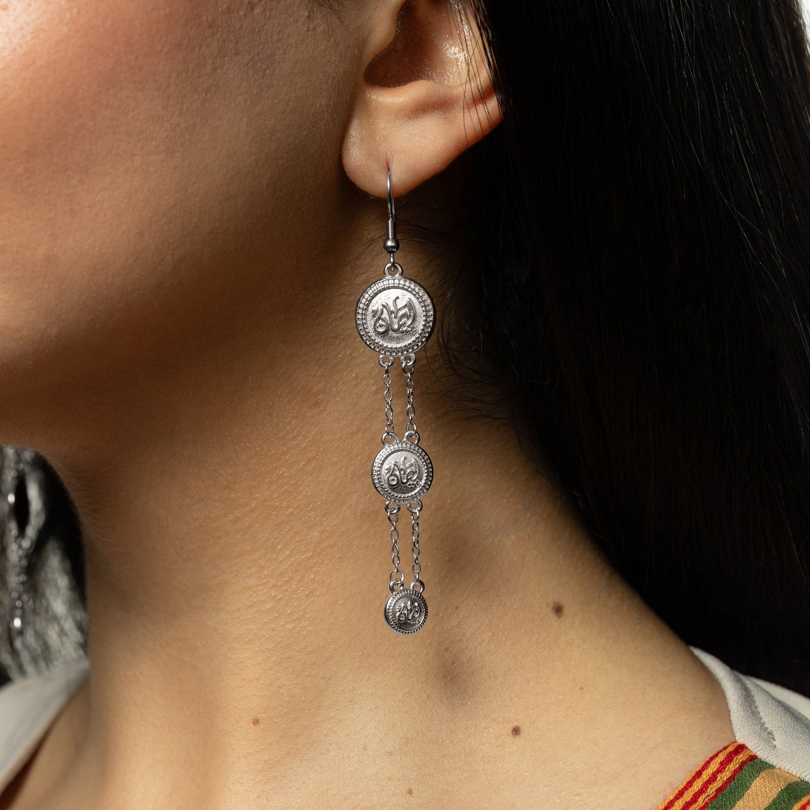Photo of the silver Iman | Faith Coin Earrings as it dangles from the model's left ear.