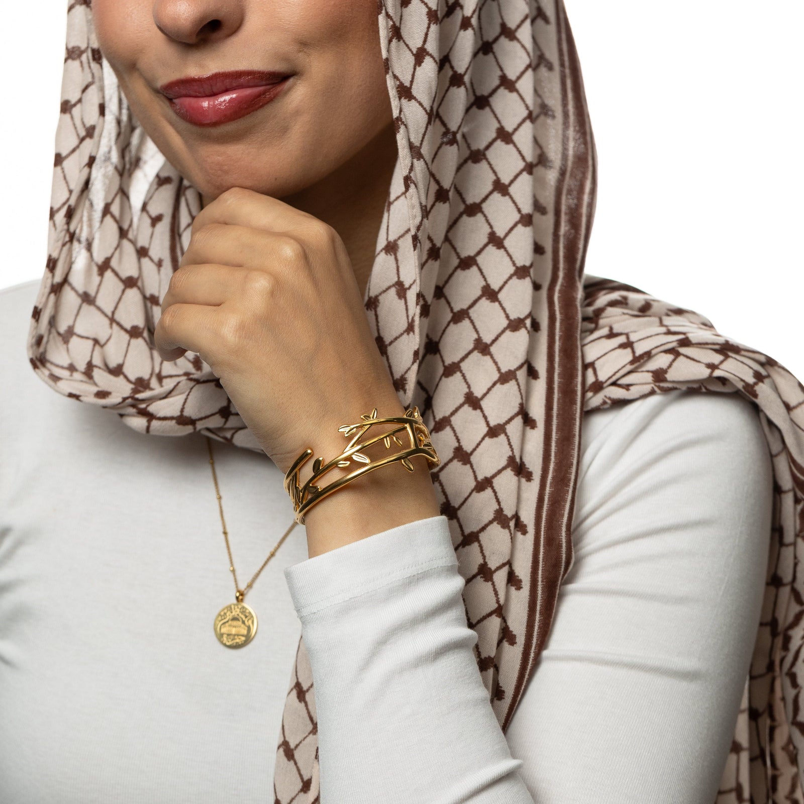 Woman with keffiyeh patterned headscarf wearing a gold Imperfect Olive Branch Cuff and a gold necklace.