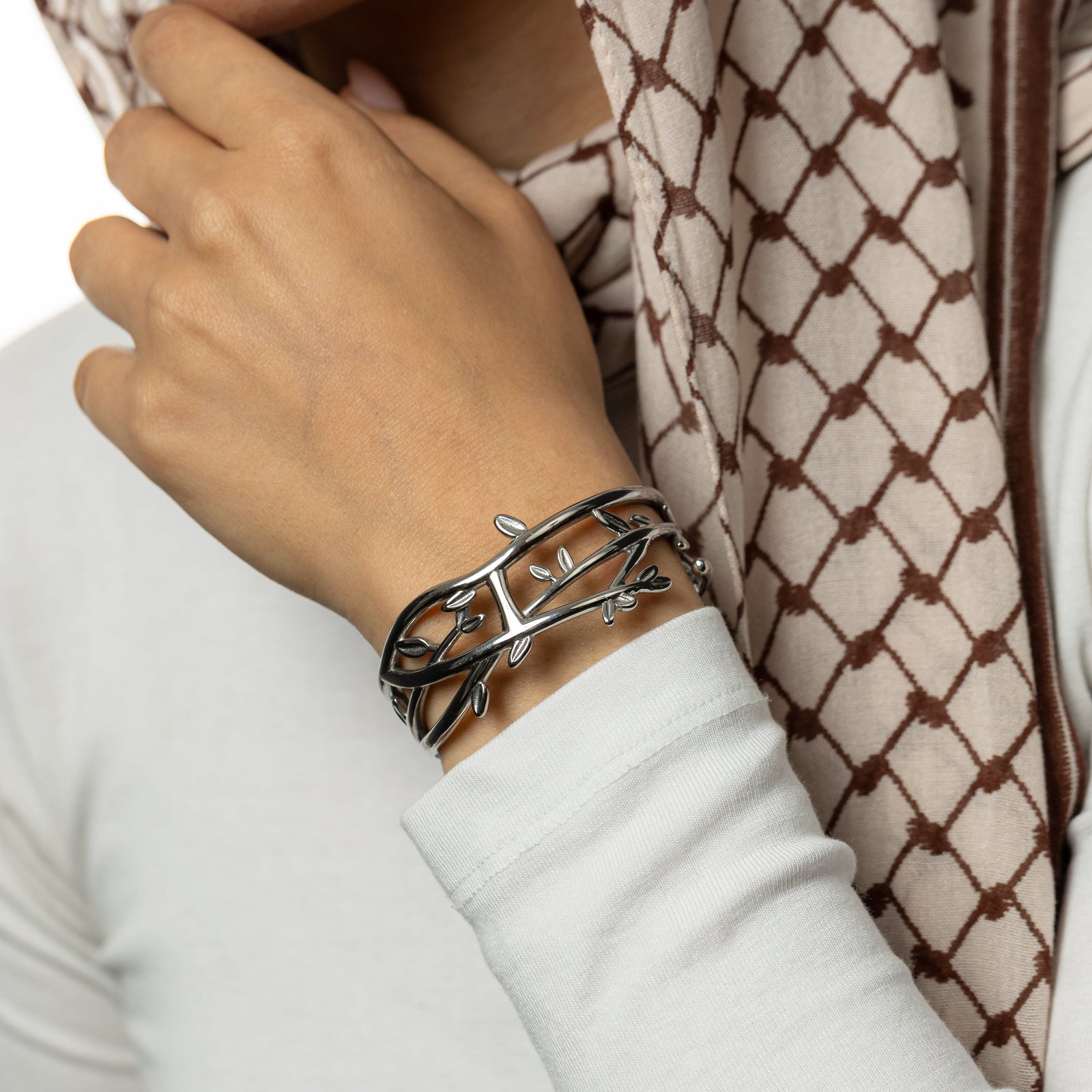 Close-up of a hand of a woman wearing a silver Imperfect Olive branch cuff with a keffiyeh patterned scarf 