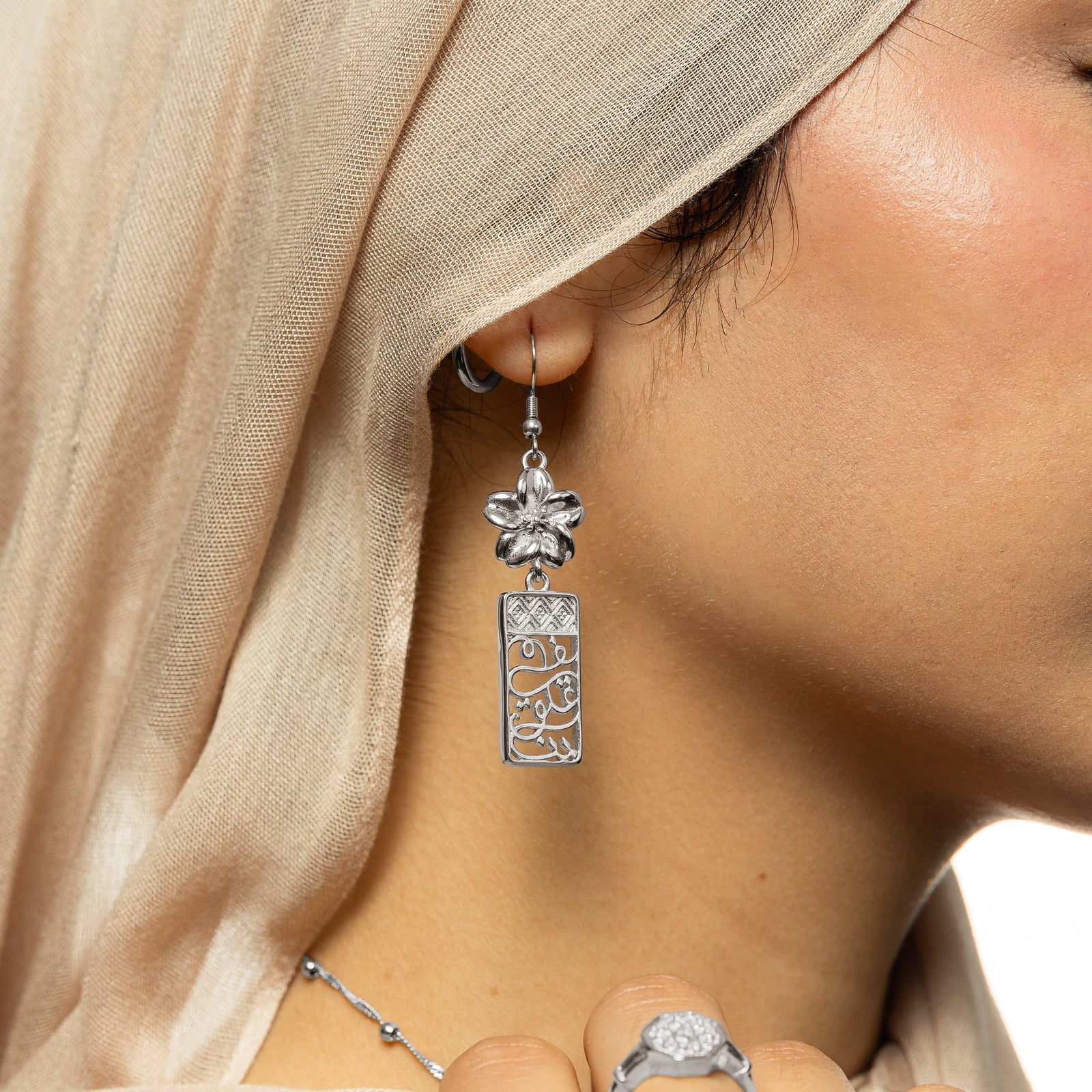 Close up the silver In Our Hearts Damascus Earrings as the model wears it on their ear.