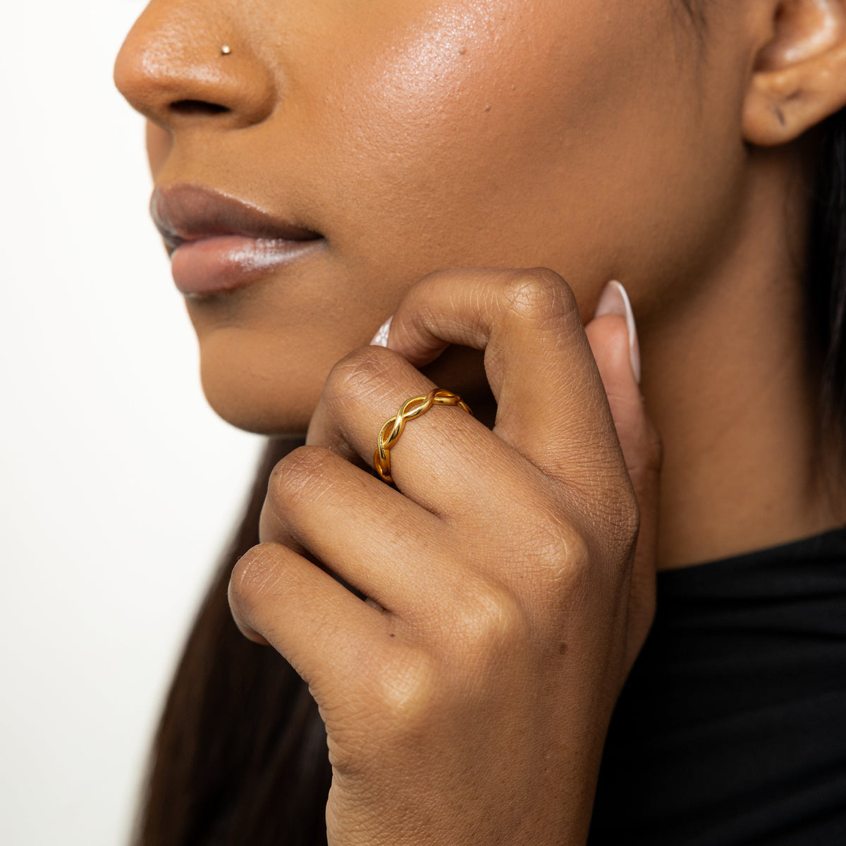 Woman wearing a gold infinity ring on her finger, hand resting near her chin.