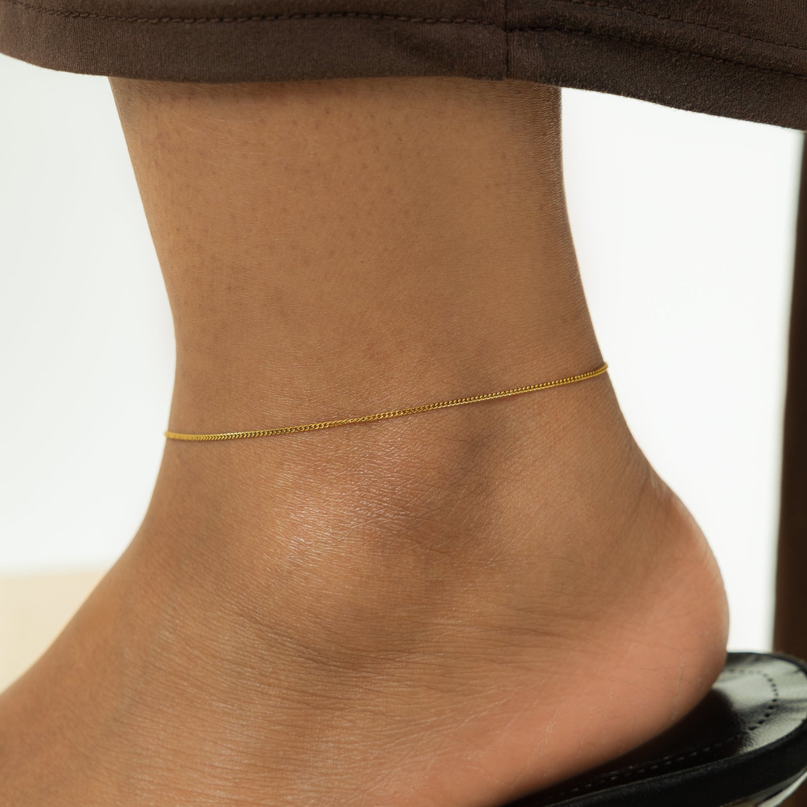 Close up of the gold Micro Curb Anklet on the model's left ankle